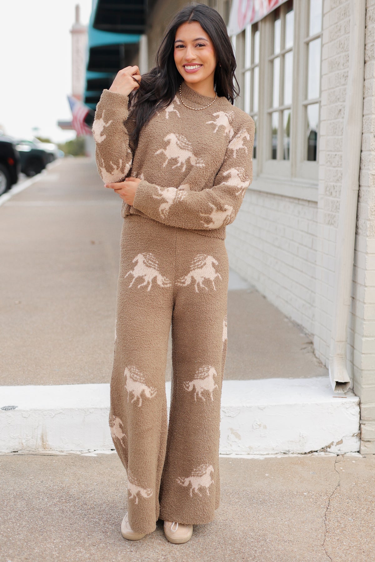 Brunette model wearing Bridlebrook Running Horse Sweater in Mocha featuring a fuzzy textured knit, cream running horse pattern, crew neckline, and long sleeves. it is paired with the Bridlebrook Running Horse Pants with the same pattern to make a set. Southern House Clothing