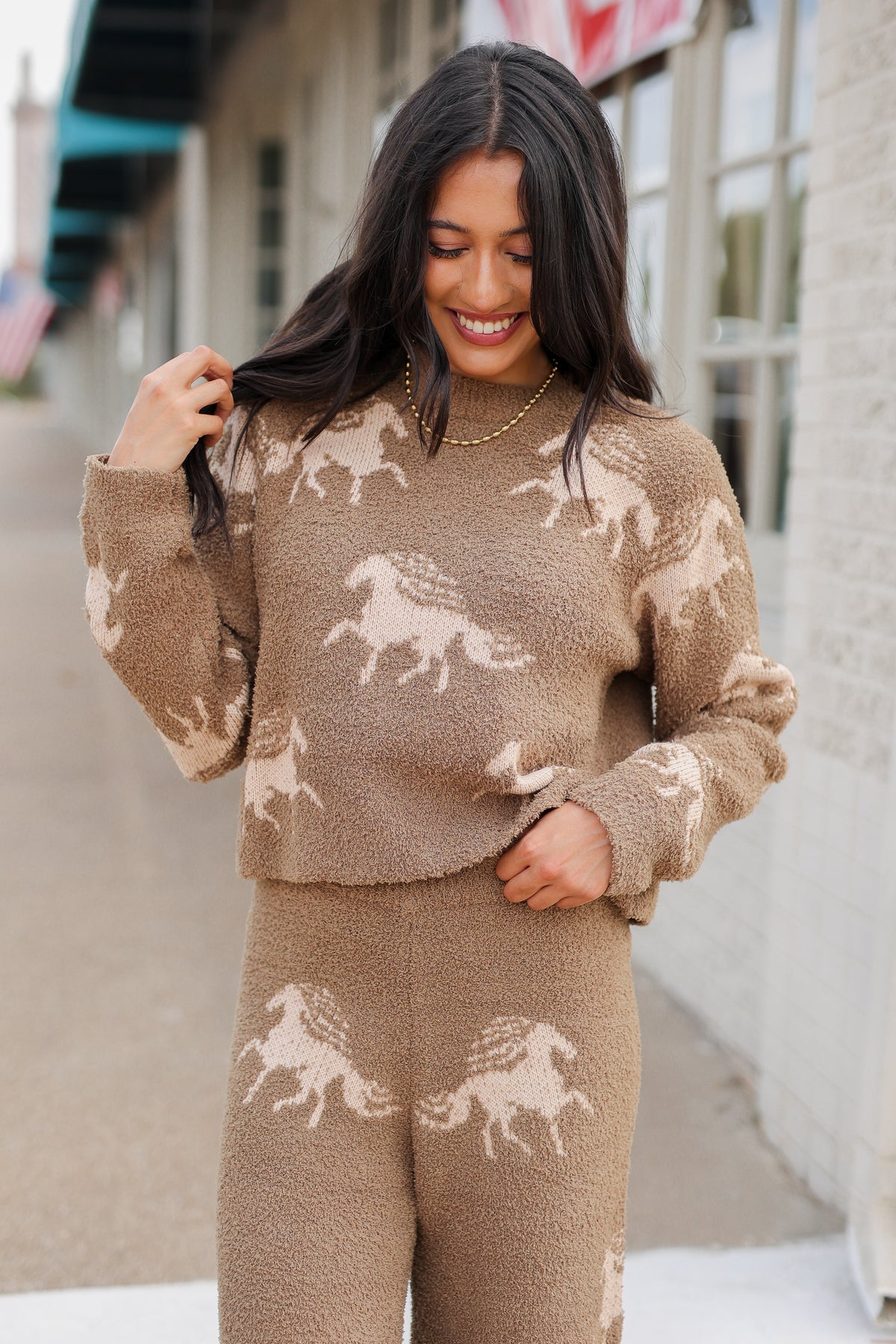 Brunette model wearing Bridlebrook Running Horse Sweater in Mocha featuring a fuzzy textured knit, cream running horse pattern, crew neckline, and long sleeves. it is paired with the Bridlebrook Running Horse Pants with the same pattern to make a set. Southern House Clothing
