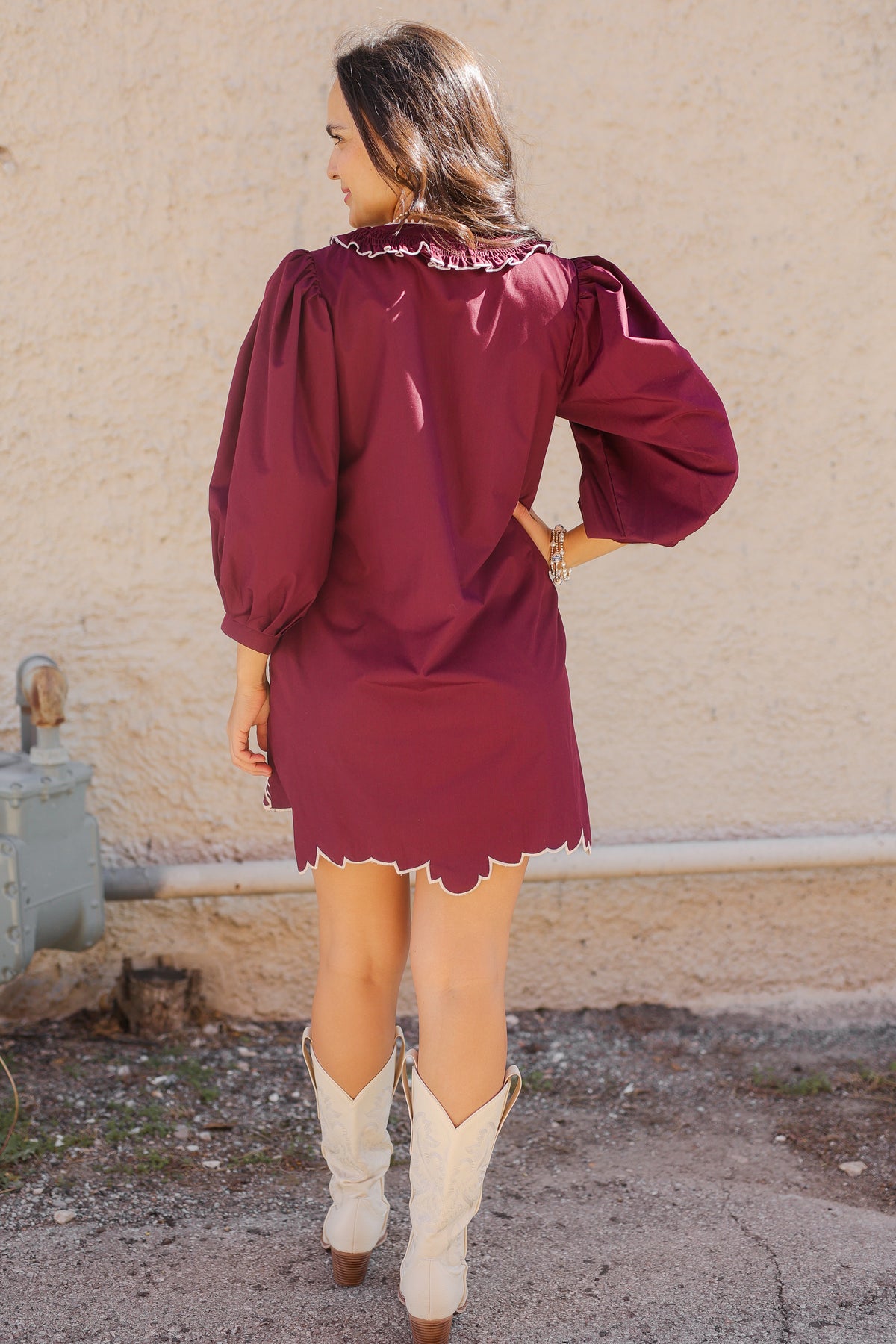 Woman wearing a burgundy dress with long sleeves and a skirt, standing against a beige wall.
