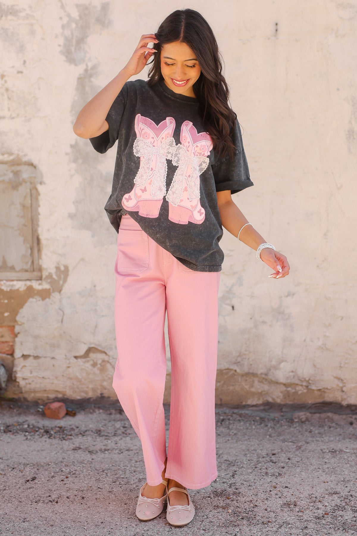 Woman wearing a black t-shirt with pink graphics and pink pants against a textured wall.