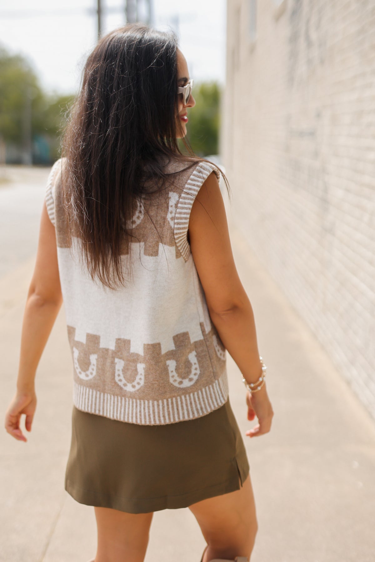 Brunette model, outside, wearing a light mocha sweater vest, tan boots, and a chocolate colored skort.
