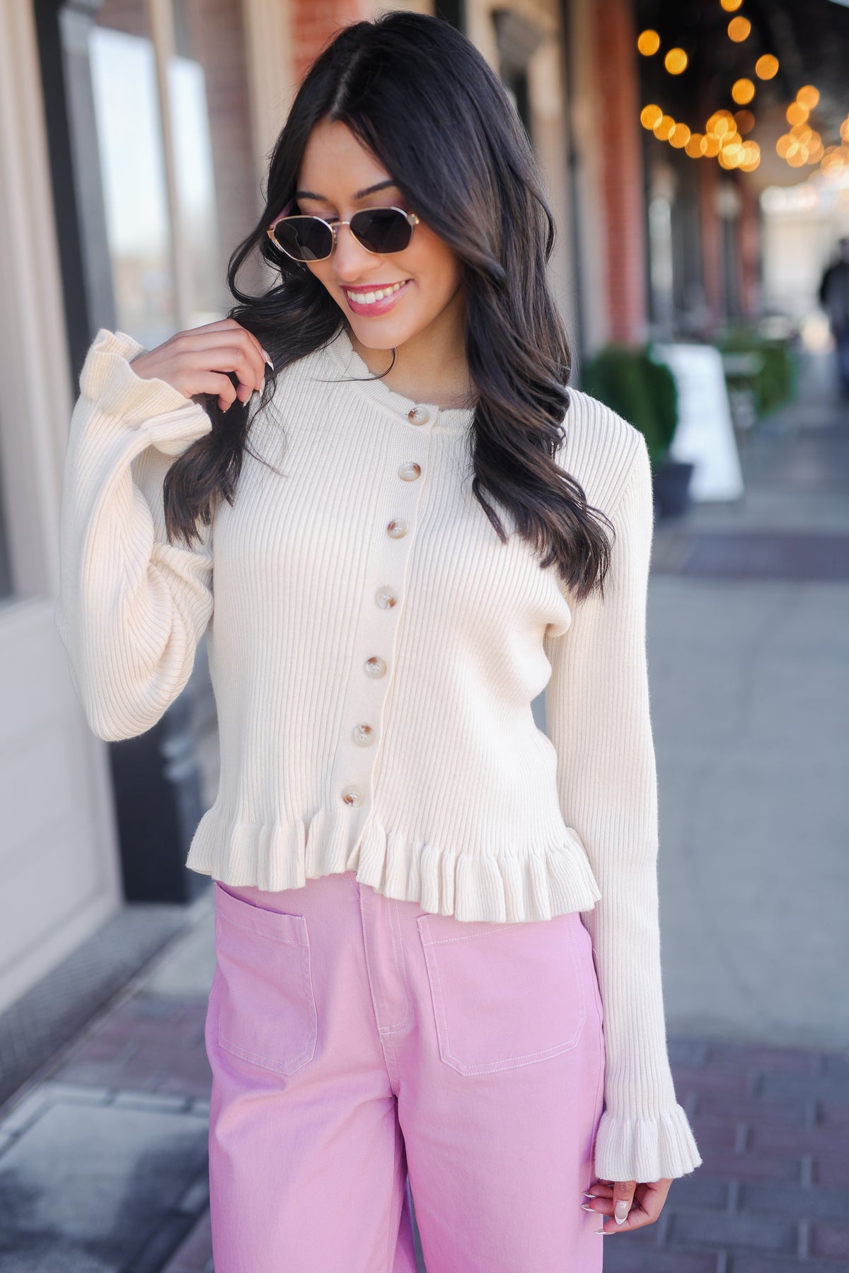 Woman wearing a cream cardigan and pink pants on a city street.