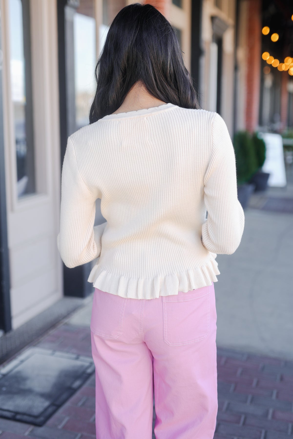 Person wearing a cream sweater with ruffled details and pink pants on a city street.