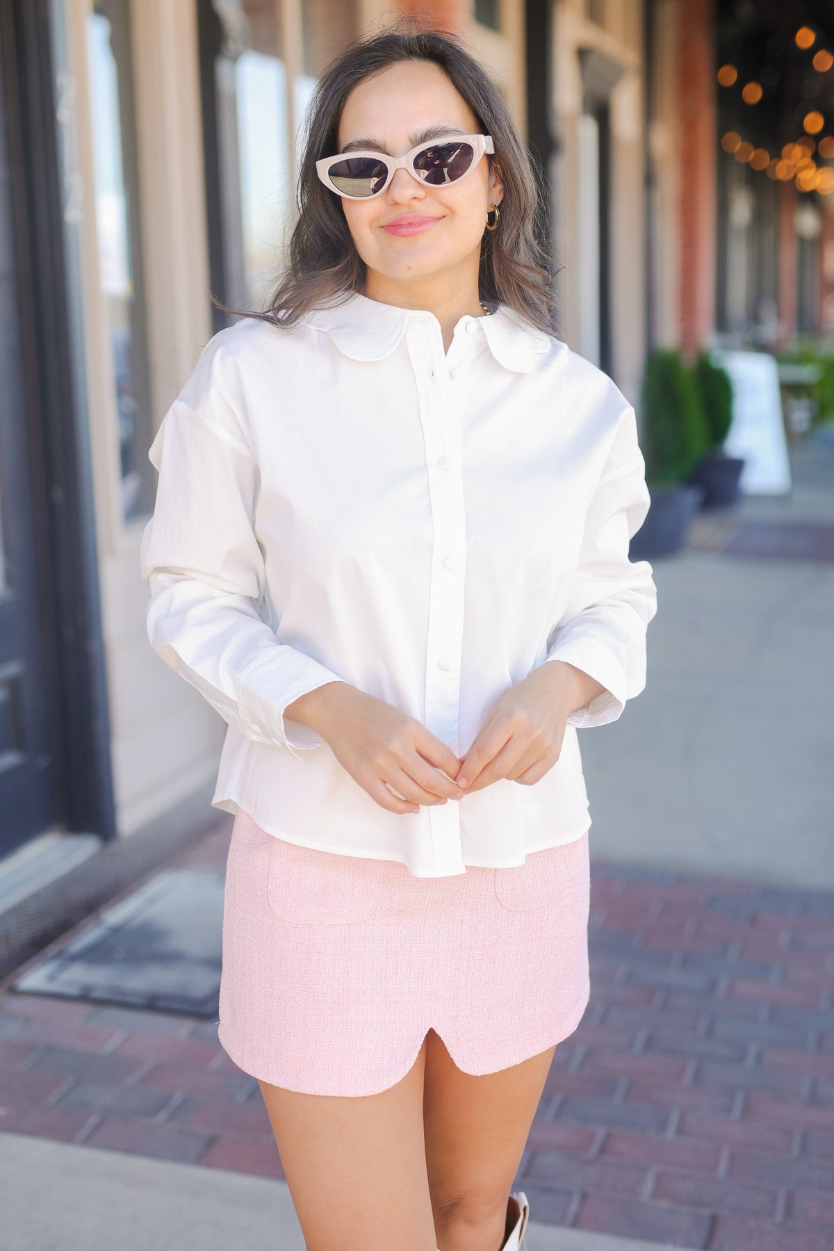 Woman wearing a white shirt and pink skirt standing on a sidewalk.