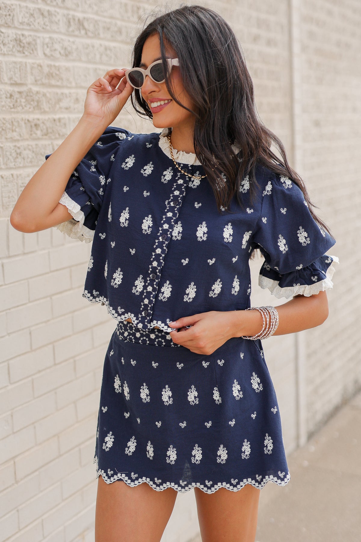 Brunette in a blue set standing outside wearing white cowboy boots and sunglasses. Southern House Clothing