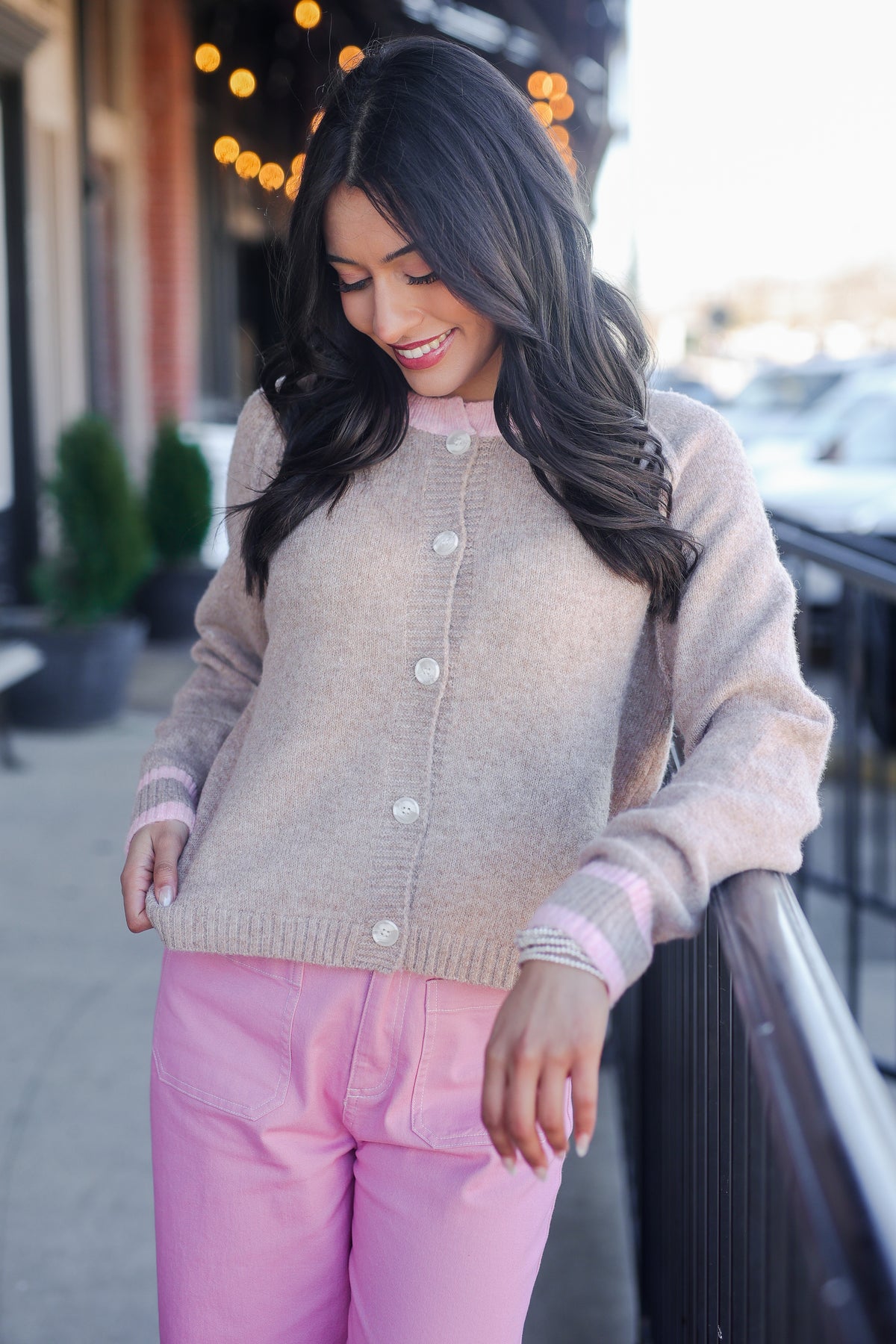 Woman wearing a beige cardigan and pink pants standing outdoors.