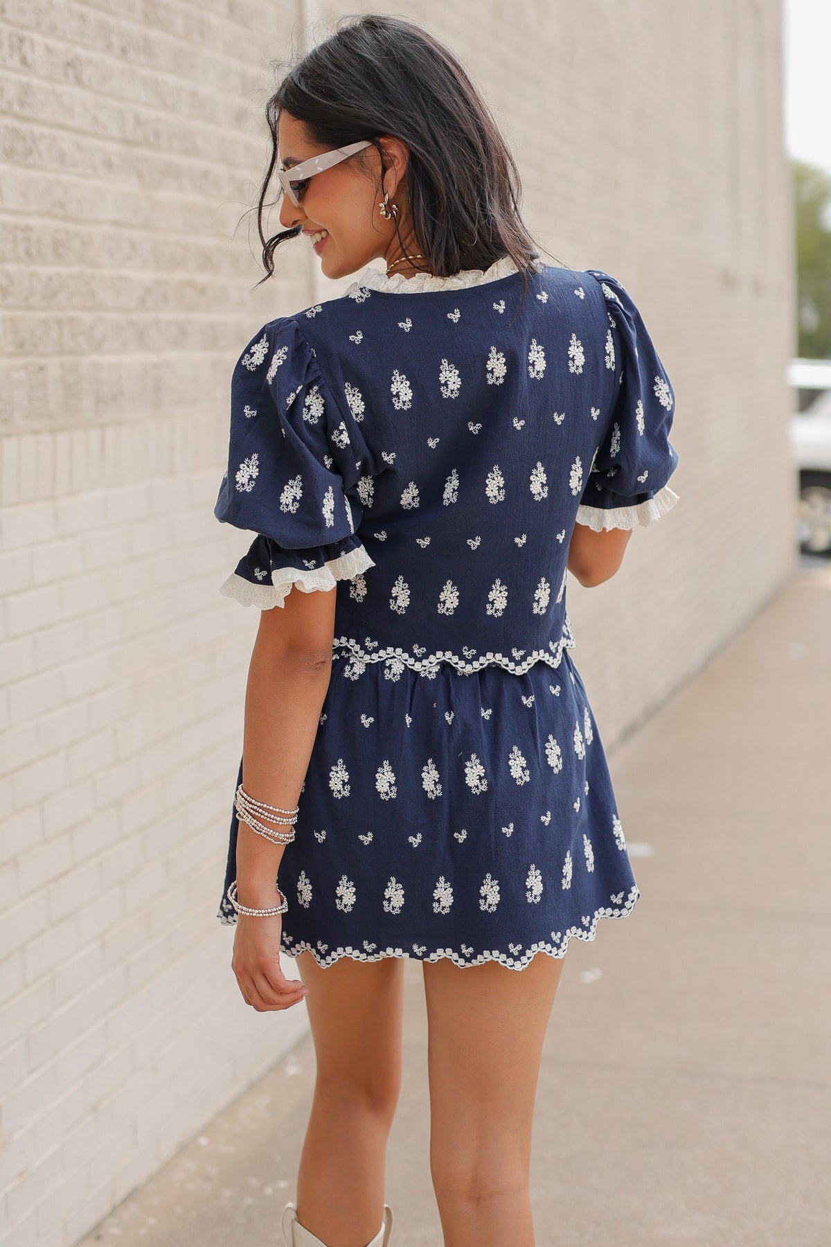 Brunette in a blue set standing outside wearing white cowboy boots and sunglasses. Southern House Clothing