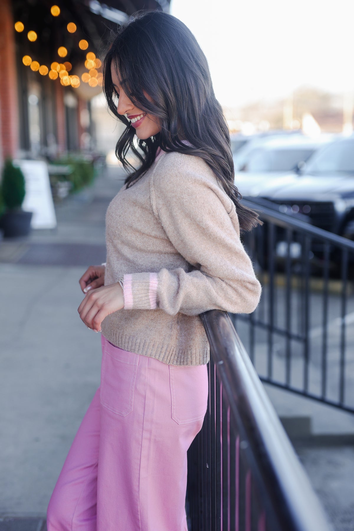 Woman wearing a beige sweater and pink pants on a city street.