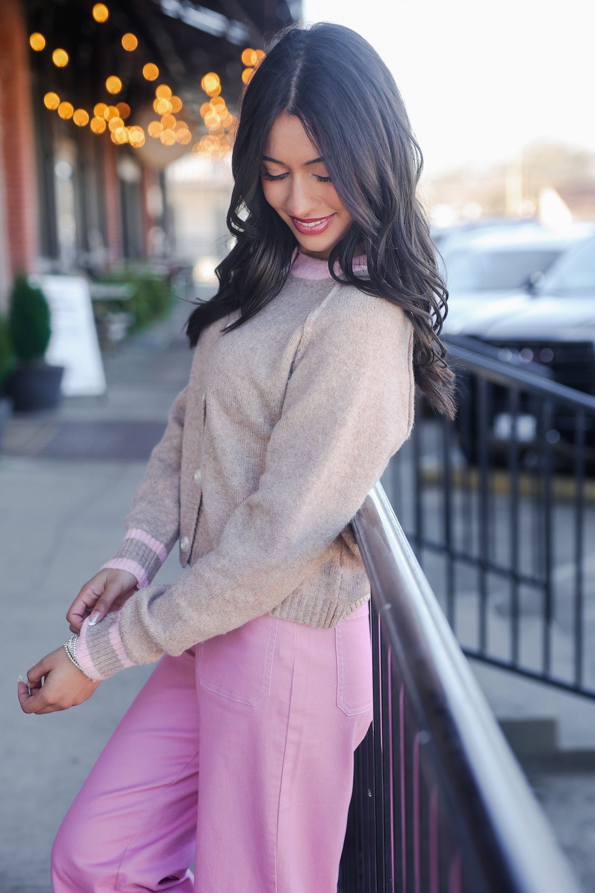 Woman wearing a beige sweater and pink pants standing on a street with blurred background