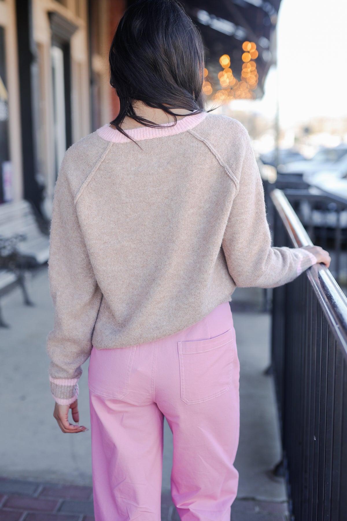 Person wearing a beige sweater and pink pants standing on a street.
