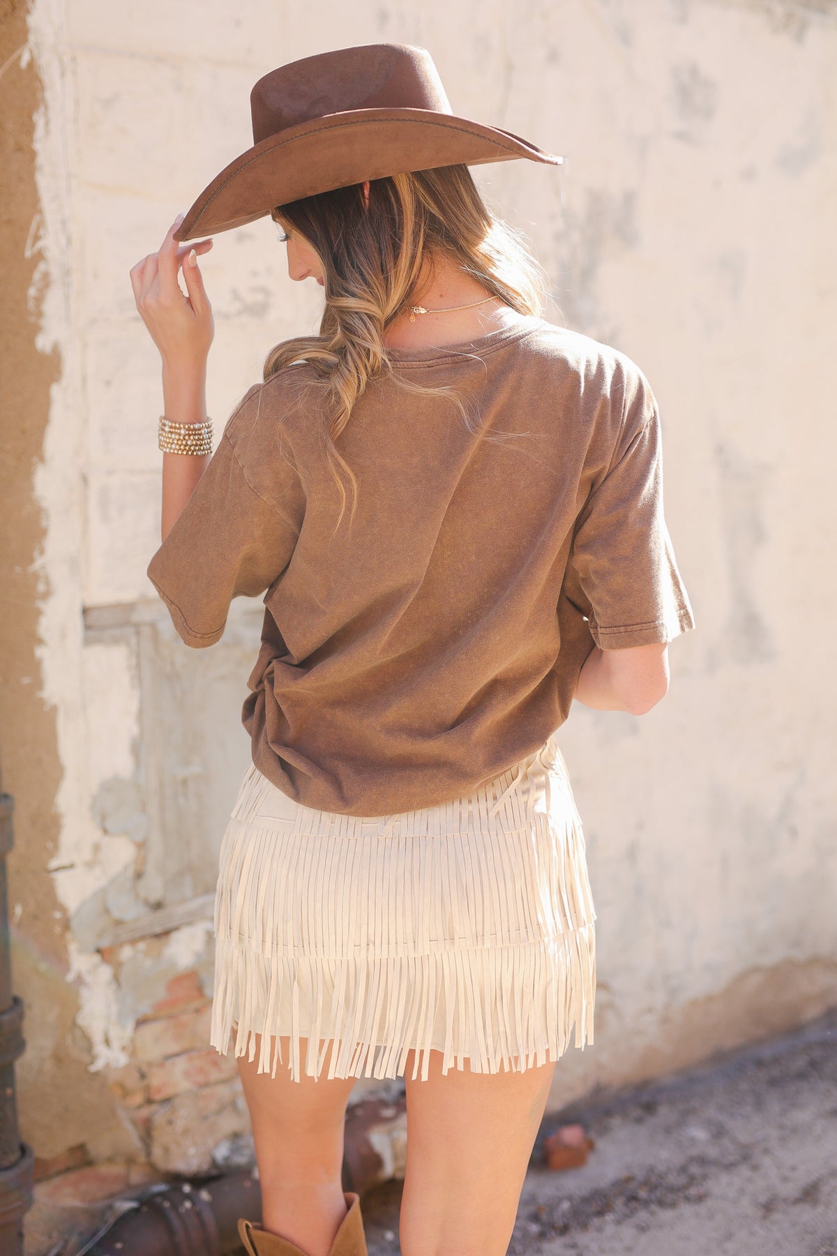 Woman wearing a brown fringed dress and hat in an outdoor setting