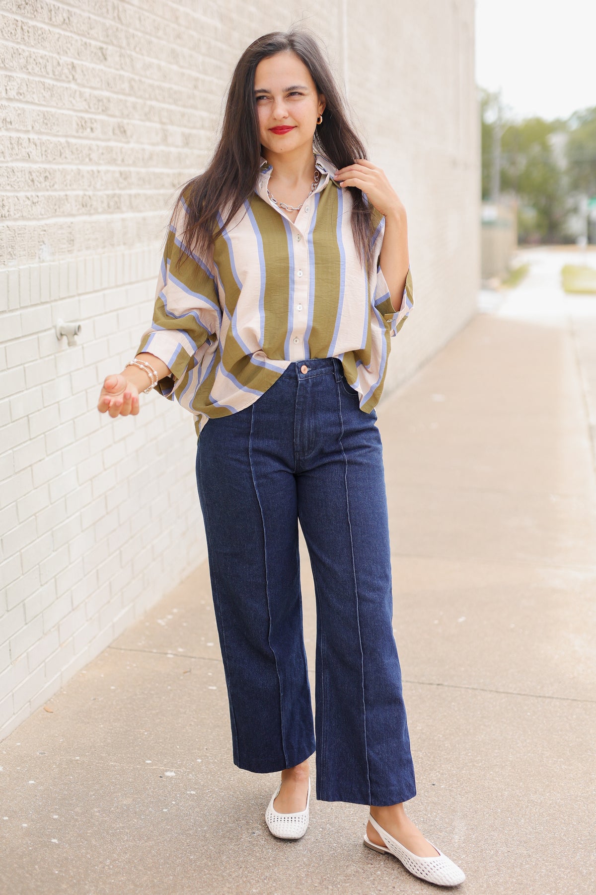 Model wearing Mabank Stripe Button-Up Top in olive green, ivory, and light blue with an oversized fit, collared neckline, and wide sleeves, styled with the Langley dark-wash jeans. Southern House Clothing