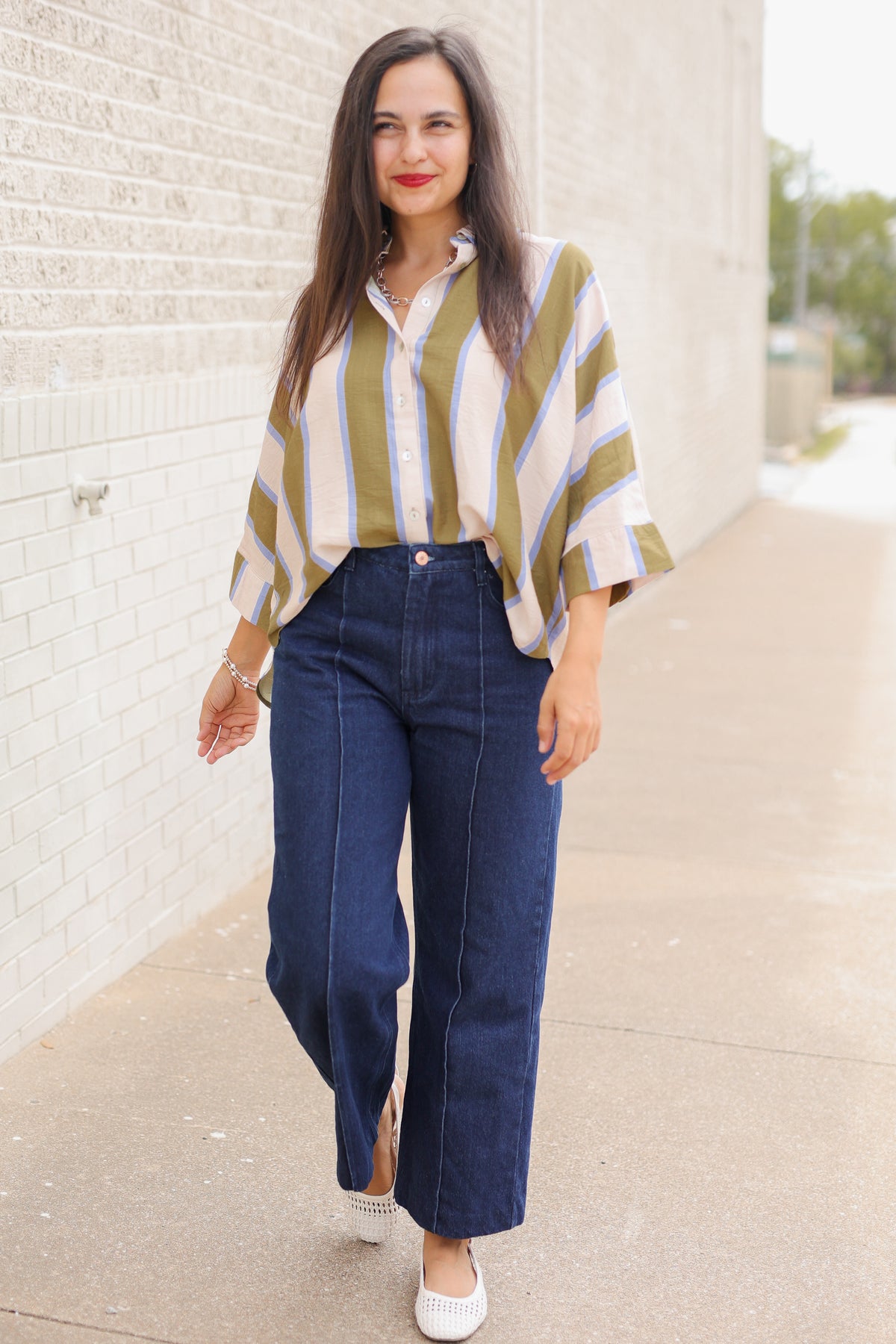 Model wearing Mabank Stripe Button-Up Top in olive green, ivory, and light blue with an oversized fit, collared neckline, and wide sleeves, styled with the Langley dark-wash jeans. Southern House Clothing