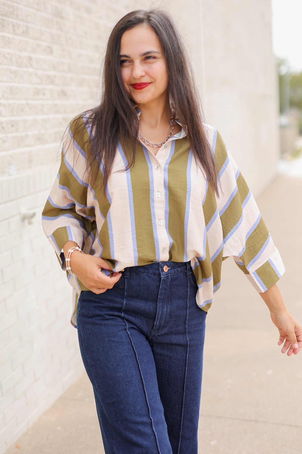Model wearing Mabank Stripe Button-Up Top in olive green, ivory, and light blue with an oversized fit, collared neckline, and wide sleeves, styled with the Langley dark-wash jeans. Southern House Clothing