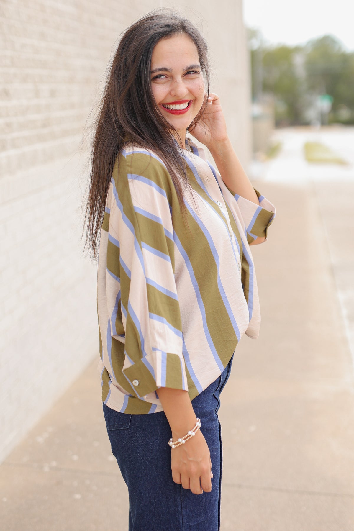 Model wearing Mabank Stripe Button-Up Top in olive green, ivory, and light blue with an oversized fit, collared neckline, and wide sleeves, styled with the Langley dark-wash jeans. Southern House Clothing