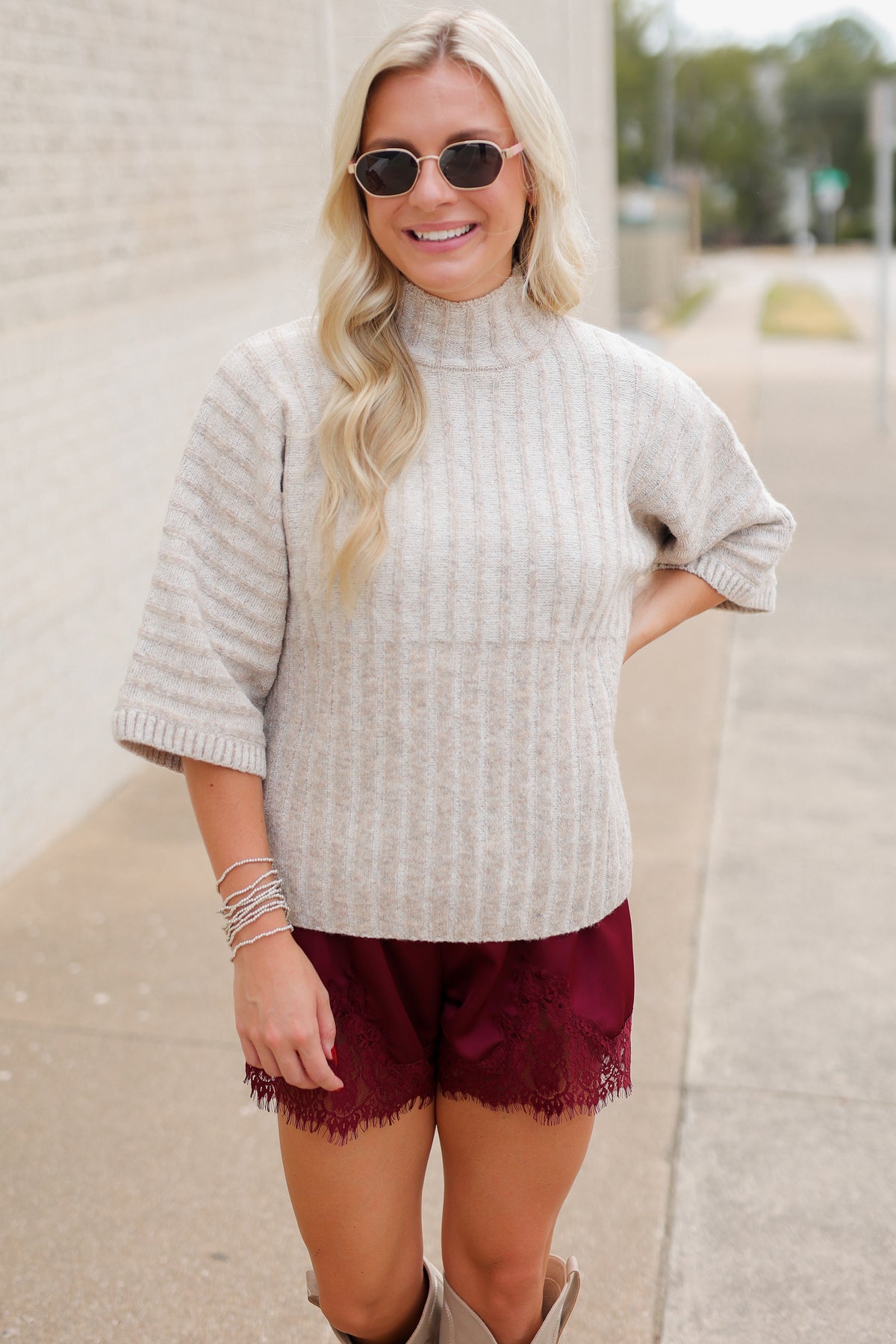 Blonde model wearing an oatmeal color sweater top and burgundy laced trimmed shorts outside. Southern House Clothing