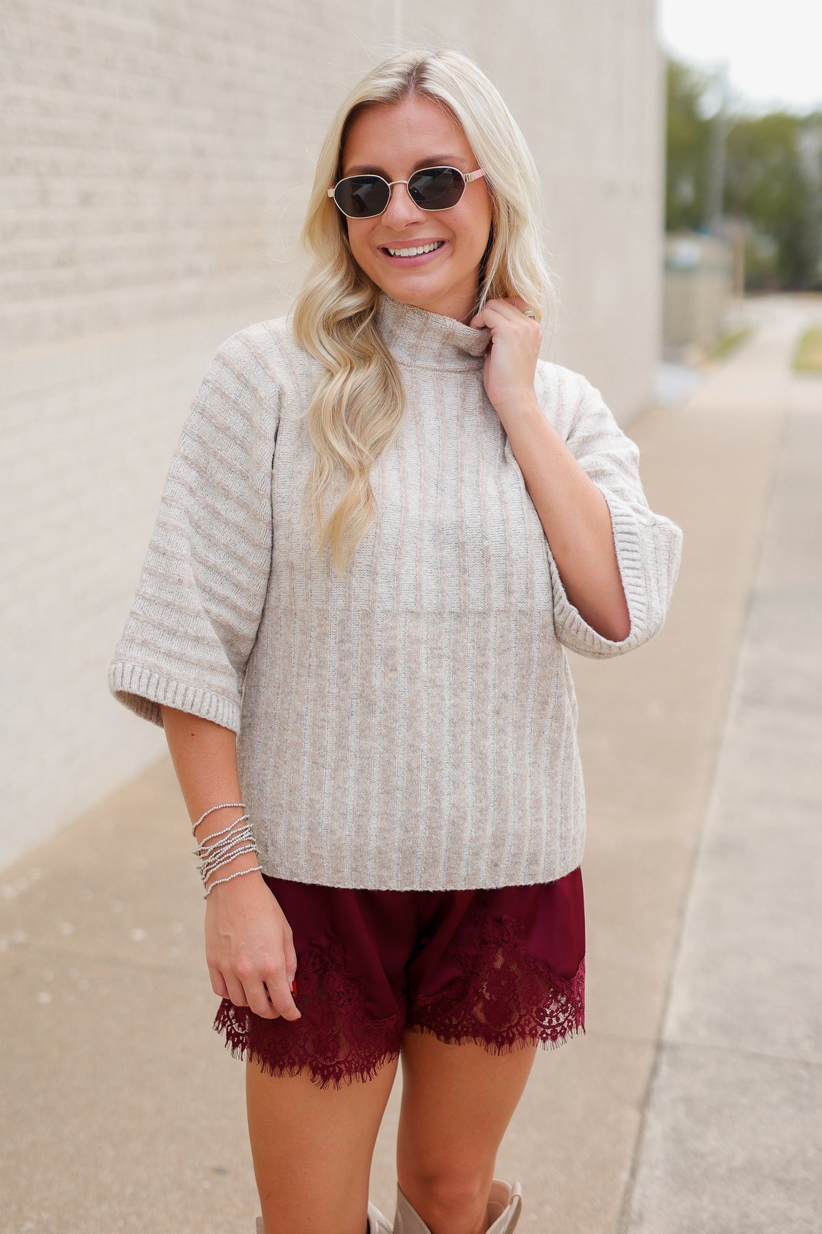 Blonde model wearing an oatmeal color sweater top and burgundy laced trimmed shorts outside. Southern House Clothing