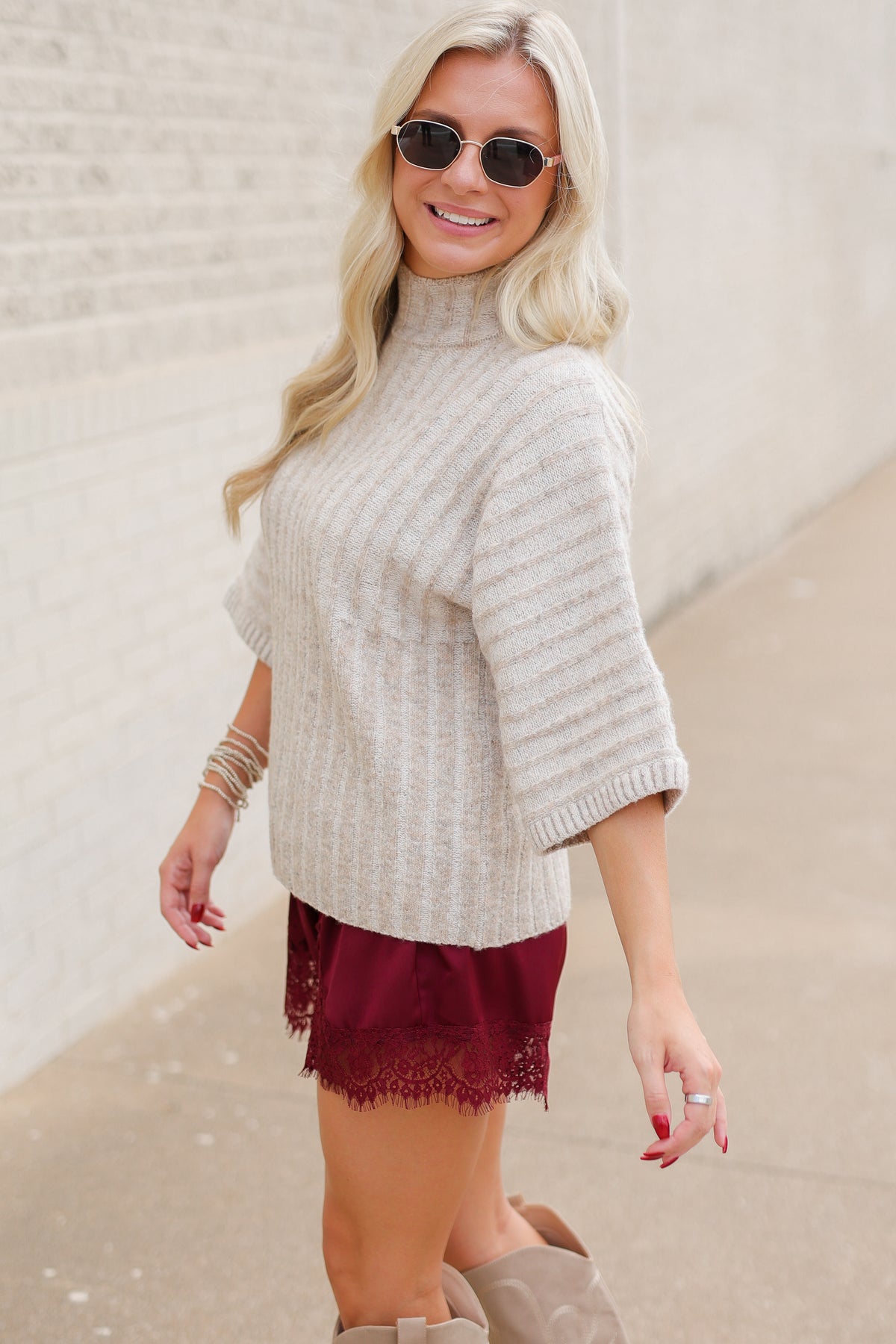 Blonde model wearing an oatmeal color sweater top and burgundy laced trimmed shorts outside. Southern House Clothing