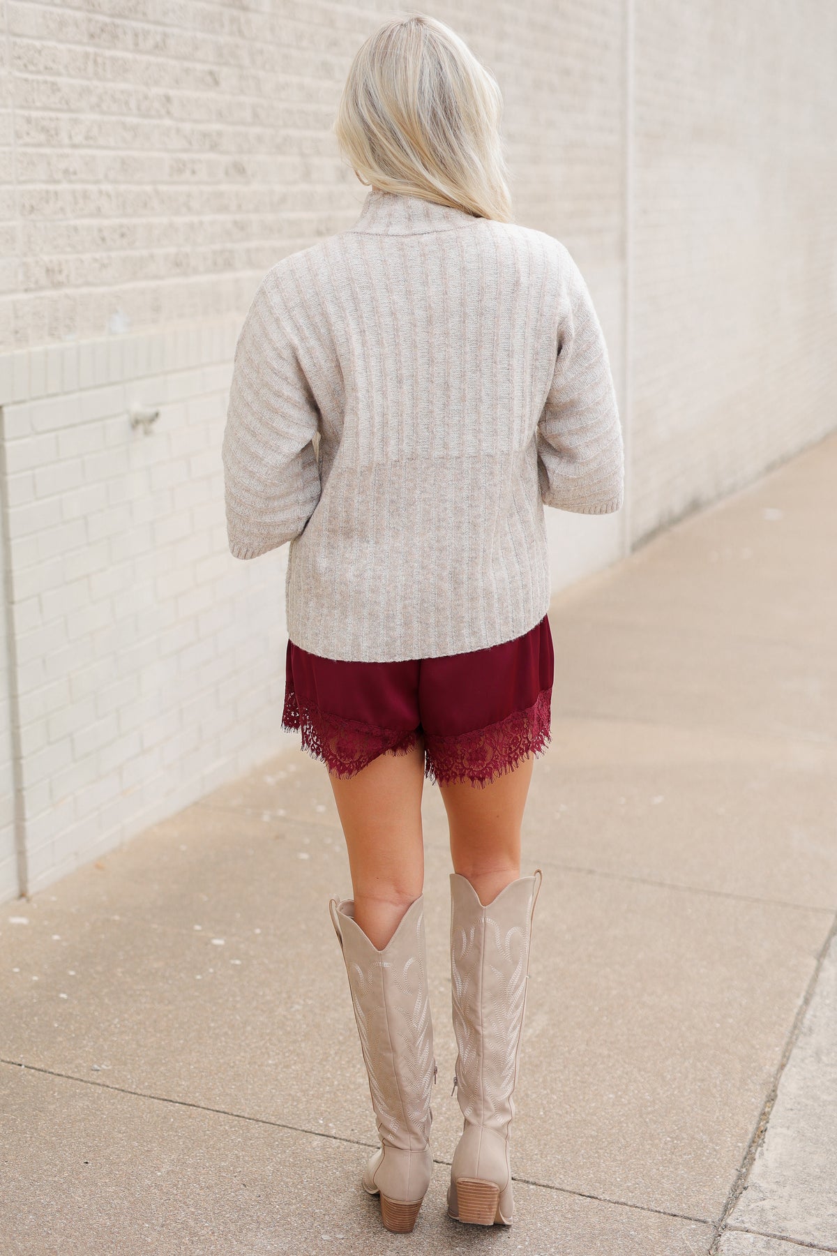 Blonde model wearing an oatmeal color sweater top and burgundy laced trimmed shorts outside. Southern House Clothing