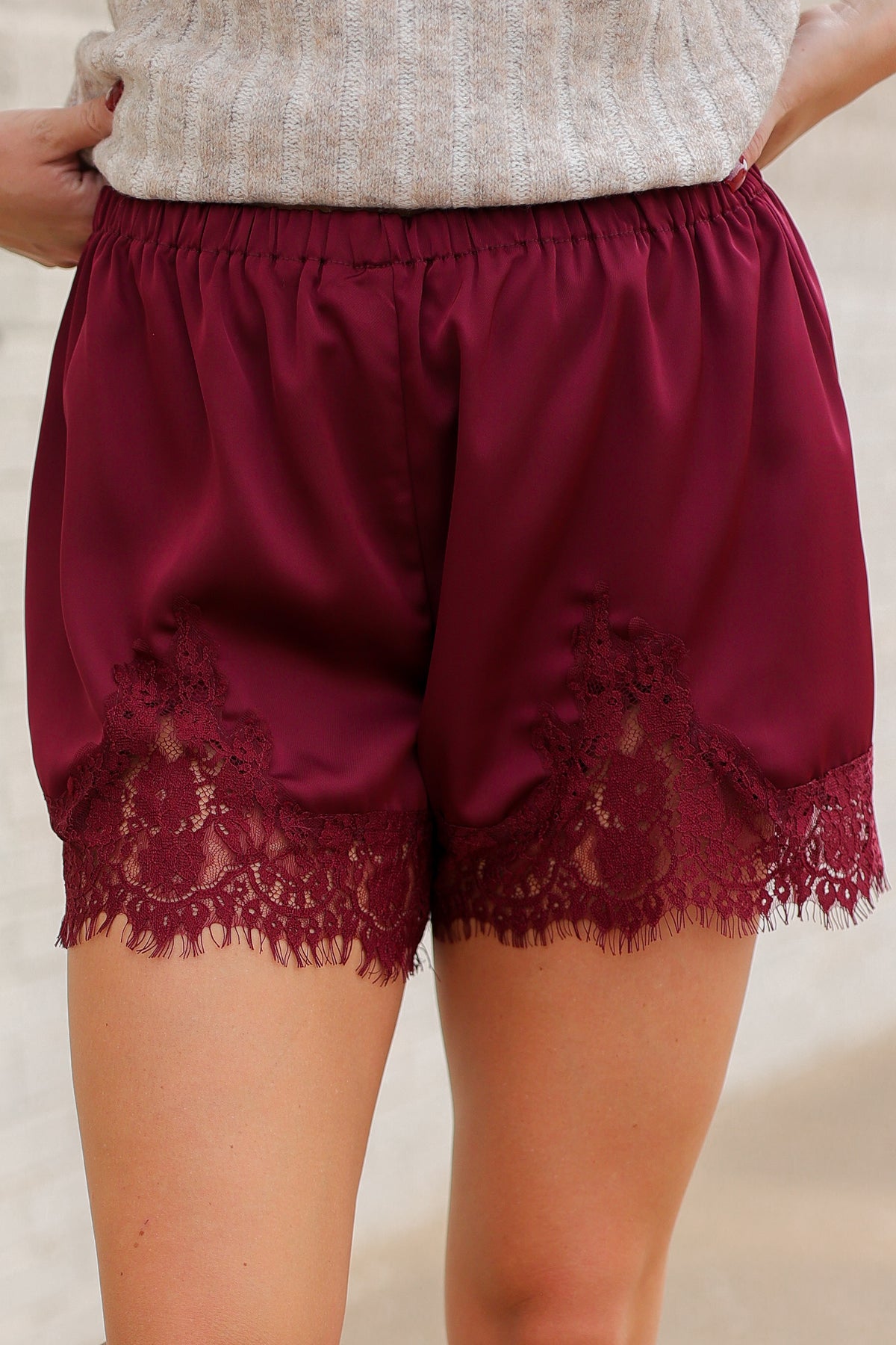 Close up of a model wearing burgundy colored laced trimmed shorts standing outside. Southern House Clothing