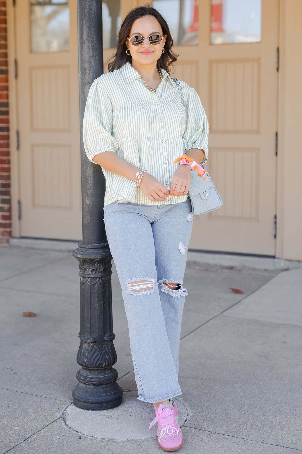 Woman in light-colored shirt and ripped jeans standing on a sidewalk next to a pole.
