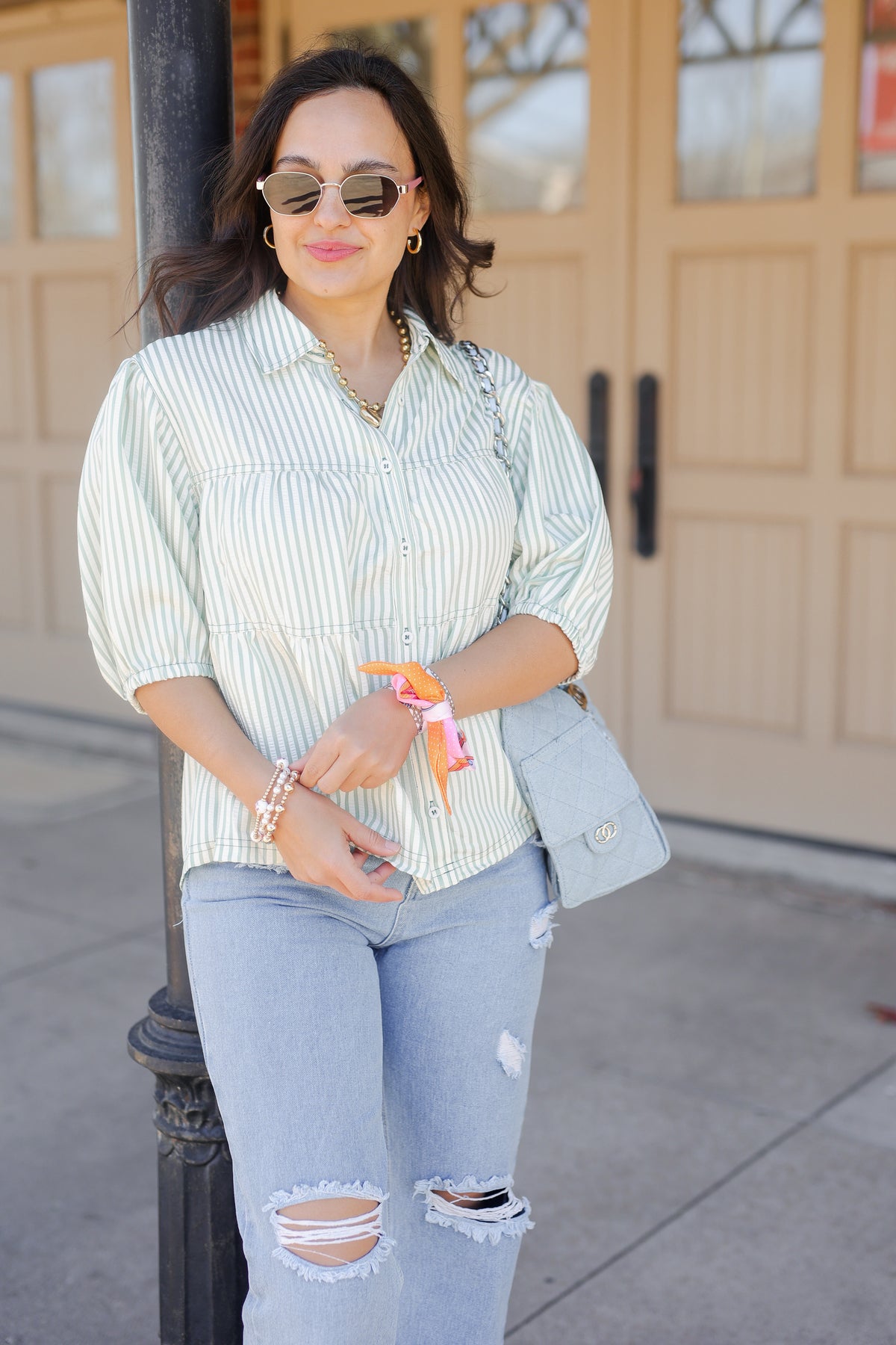 Woman wearing a striped shirt and ripped jeans standing outdoors.