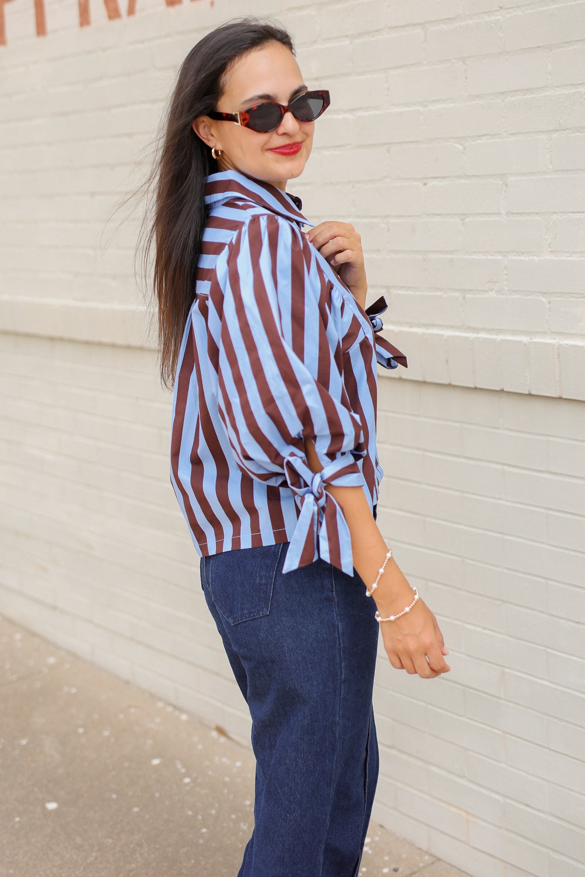 Brunette model wearing a 3/4 sleeve brown and blue blouse with denim jeans outside. Southern House Clothing.