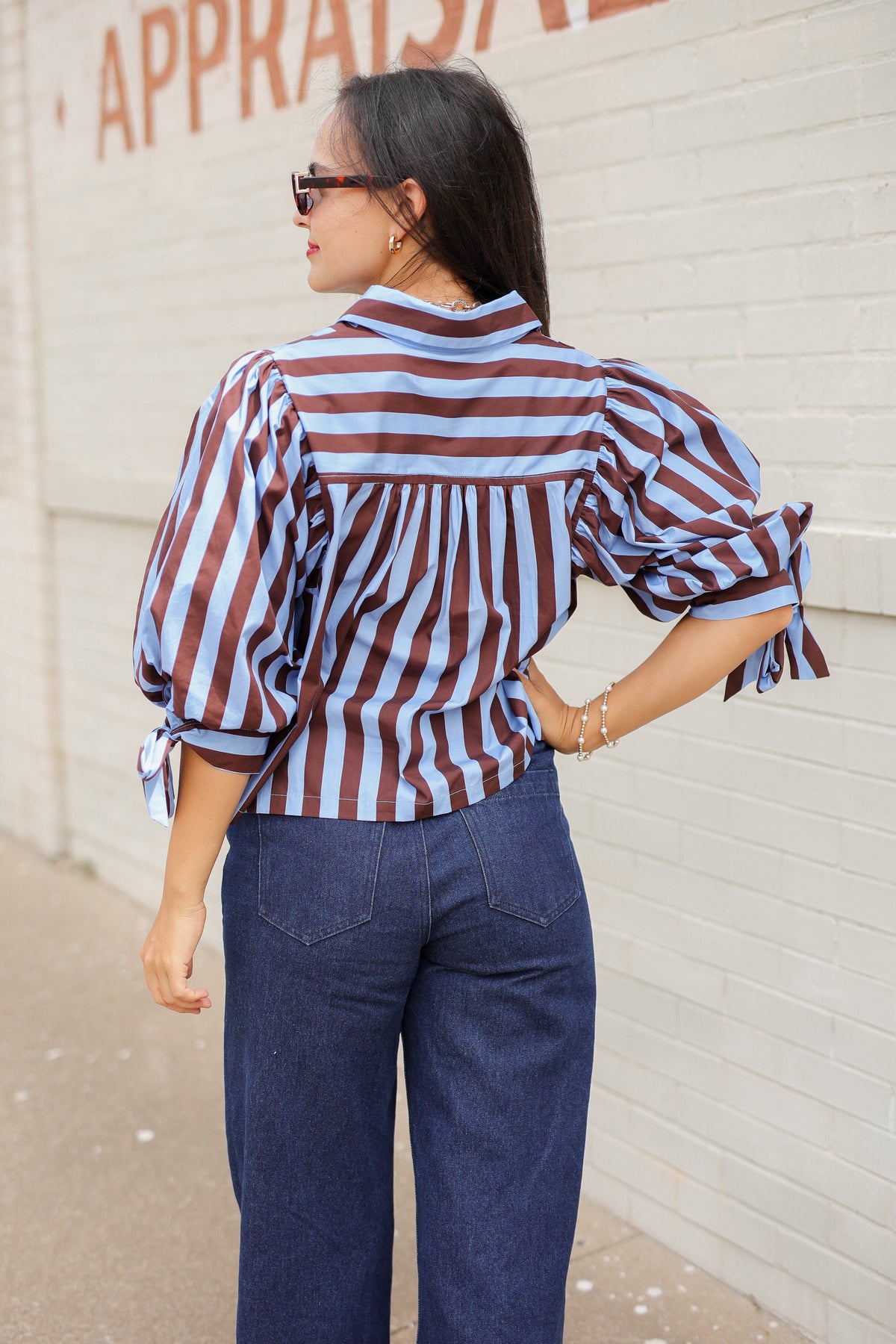 Brunette model wearing a 3/4 sleeve brown and blue blouse with denim jeans outside. Southern House Clothing.