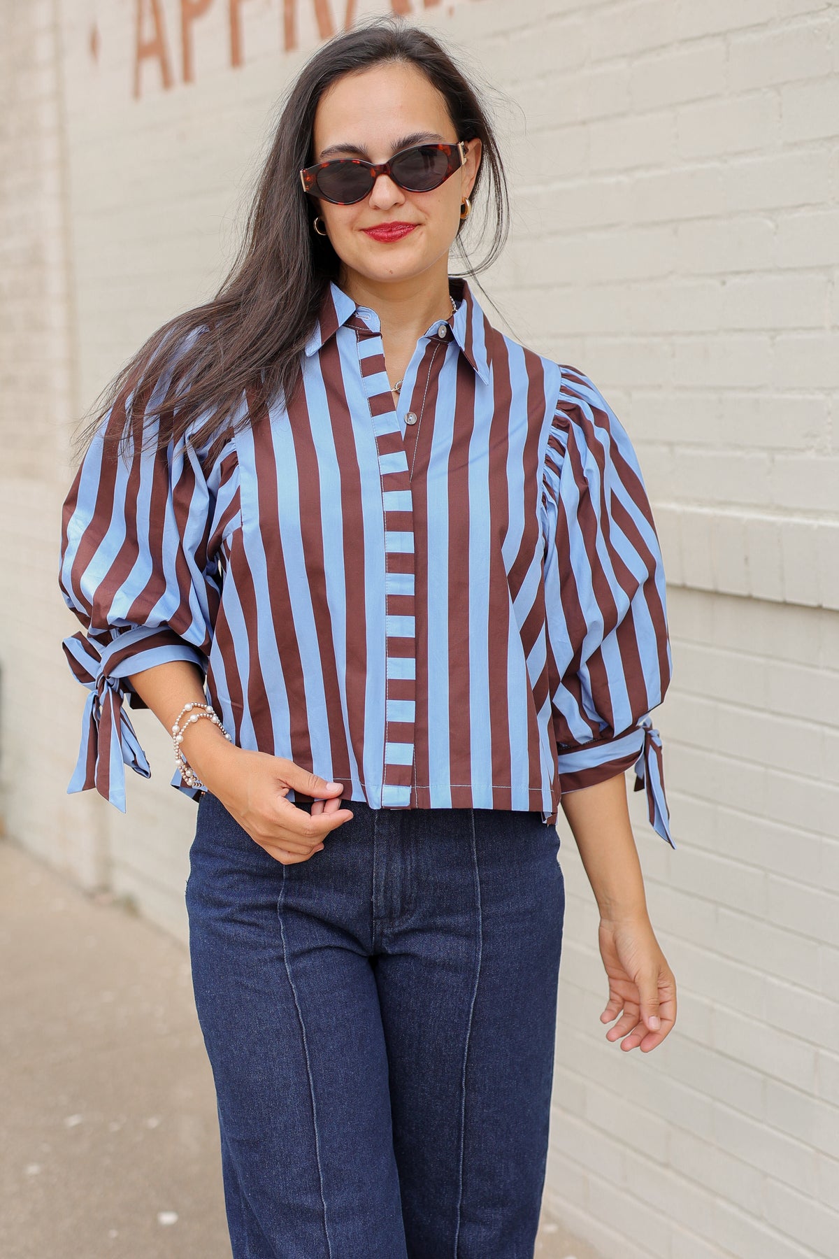 Brunette model wearing a 3/4 sleeve brown and blue blouse with denim jeans outside. Southern House Clothing.