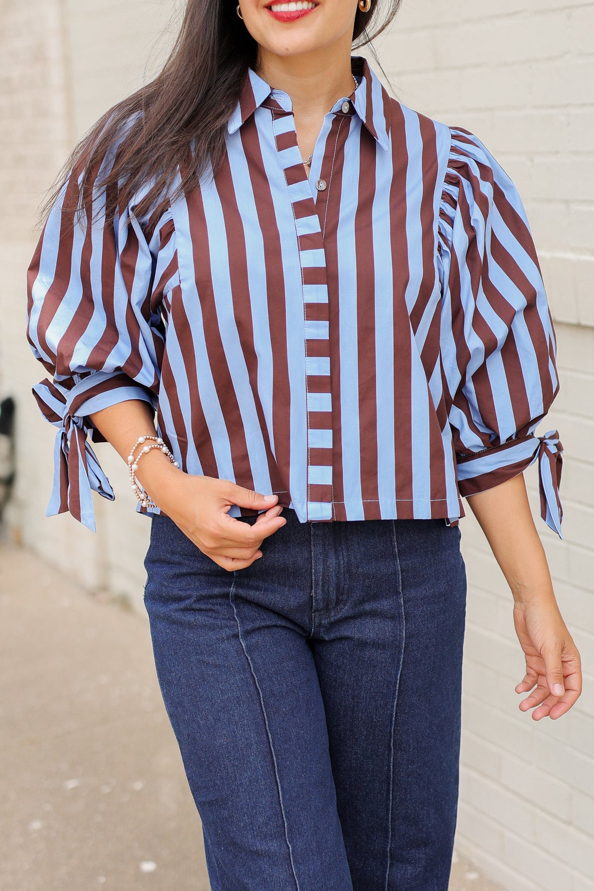 Brunette model wearing a 3/4 sleeve brown and blue blouse with denim jeans outside. Southern House Clothing.