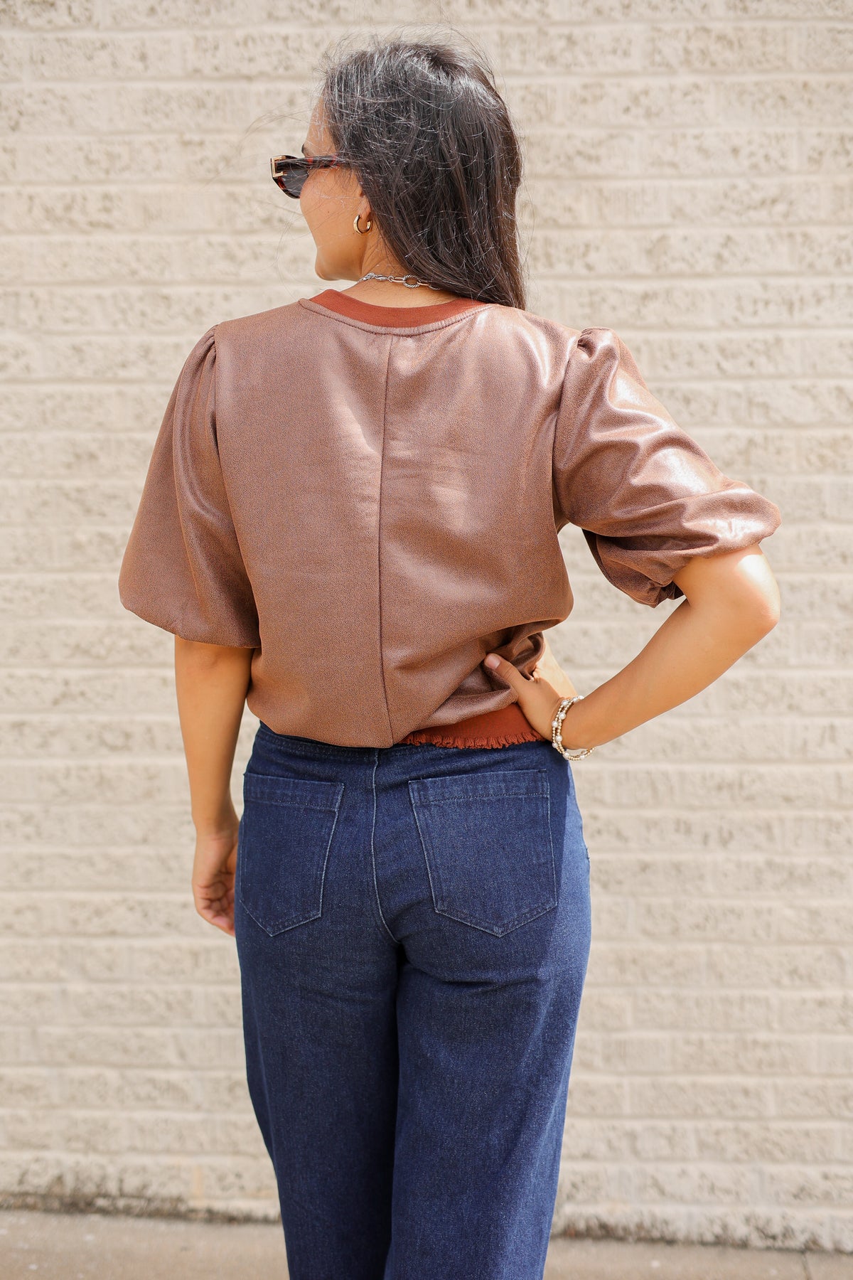 Brunette model standing outside wearing a brown blouse and denim jeans wearing black sunglasses.