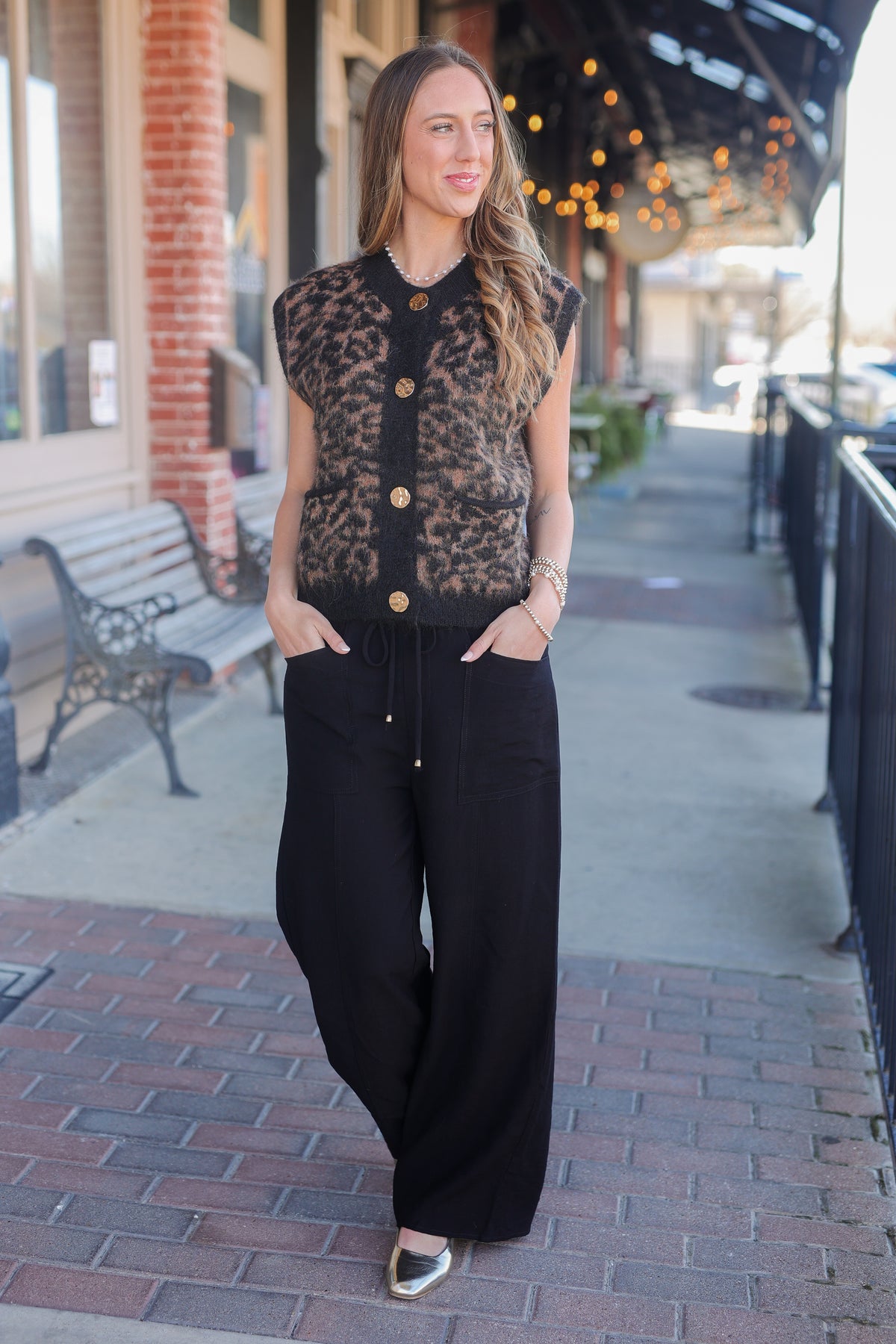 Woman wearing a leopard print vest over a black top and black pants on a sidewalk.
