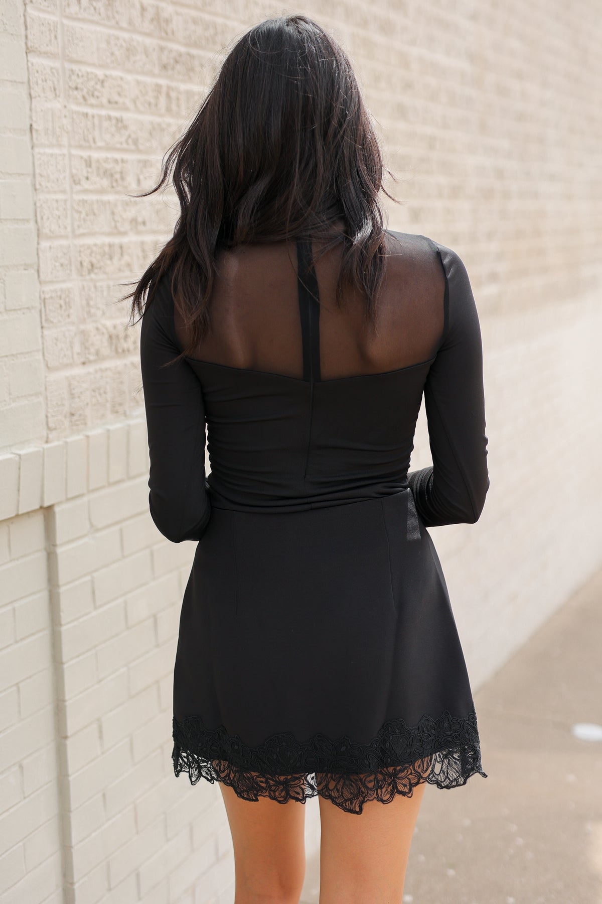 Model wearing Nocturne Mesh Panel Bodysuit in Black featuring long sleeves and sheer mesh panels, styled with Bellarose Lace Hem Mini Skort in Black and red western boots standing outside. Southern House Clothing