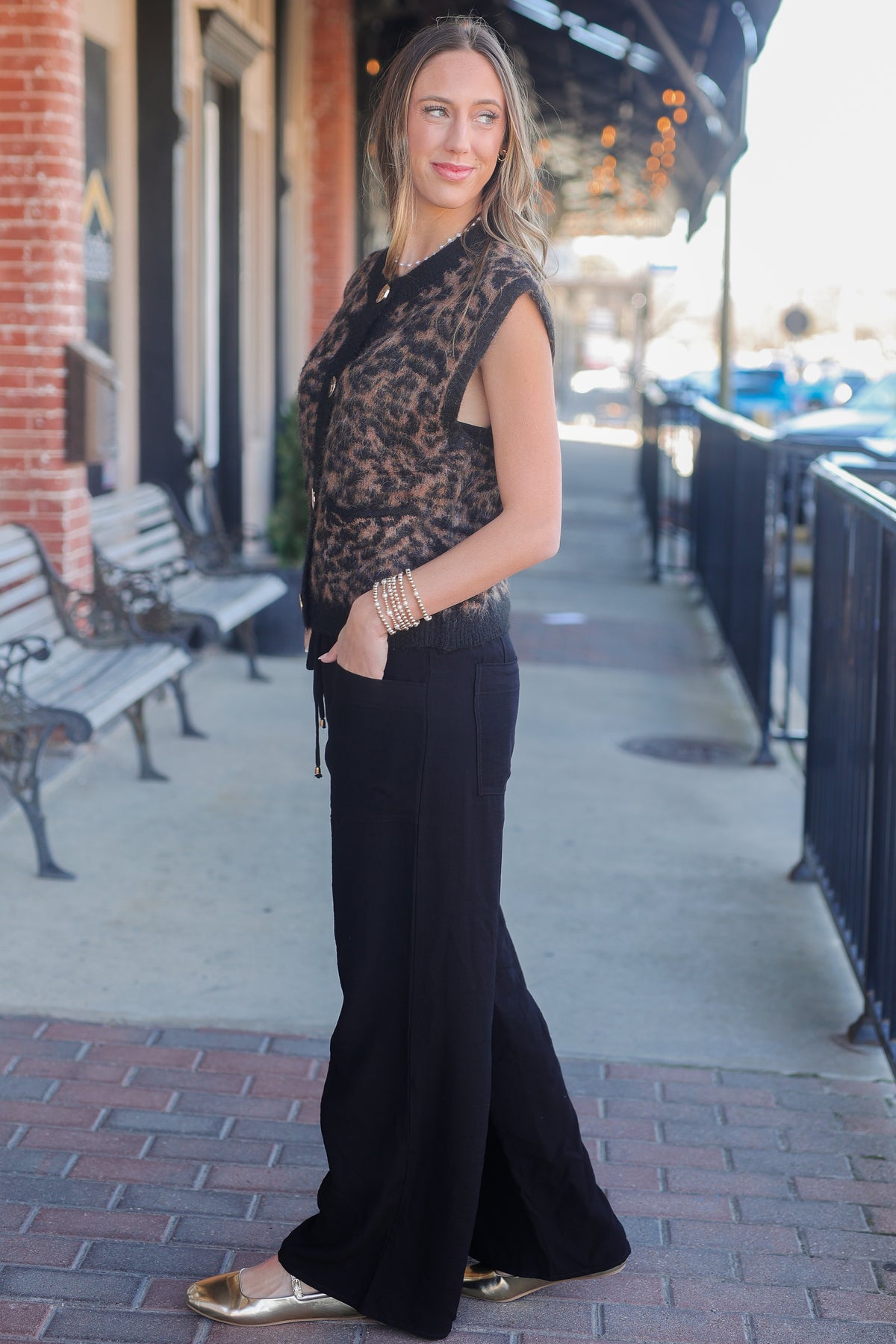 Woman in a black lace top and wide-leg pants standing on a sidewalk.