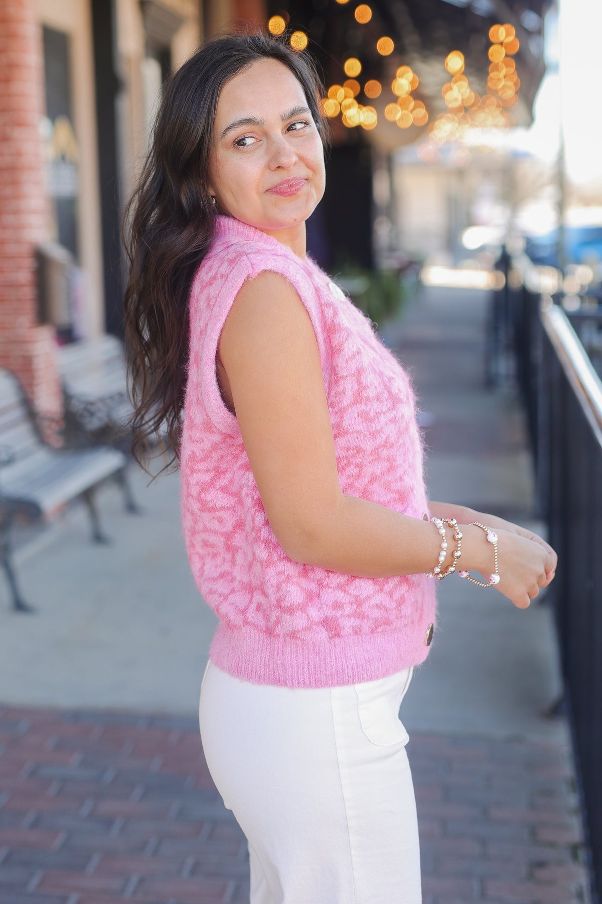 Woman wearing a pink sleeveless sweater and white pants on a city street.
