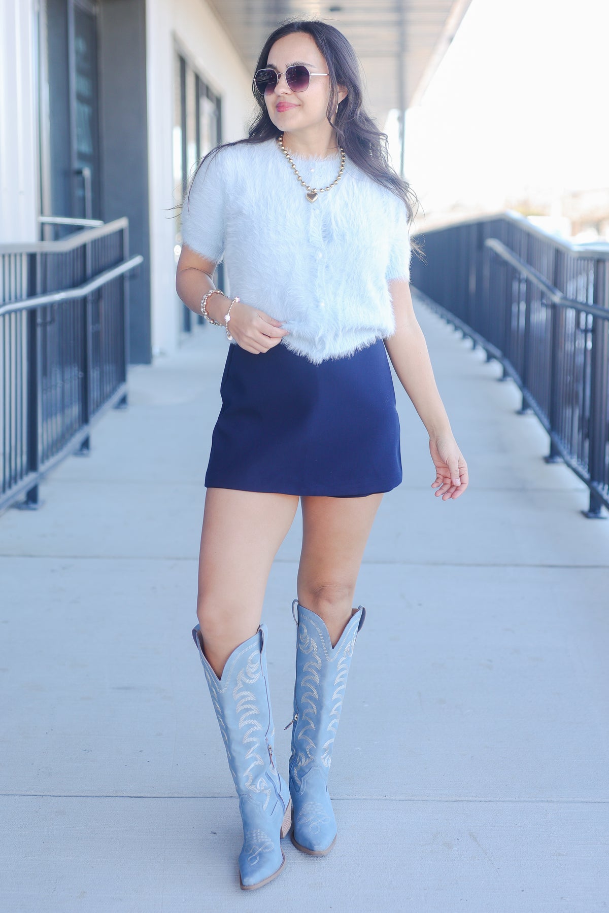 Woman wearing a light blue top, dark blue skirt, and matching blue boots on a sidewalk.