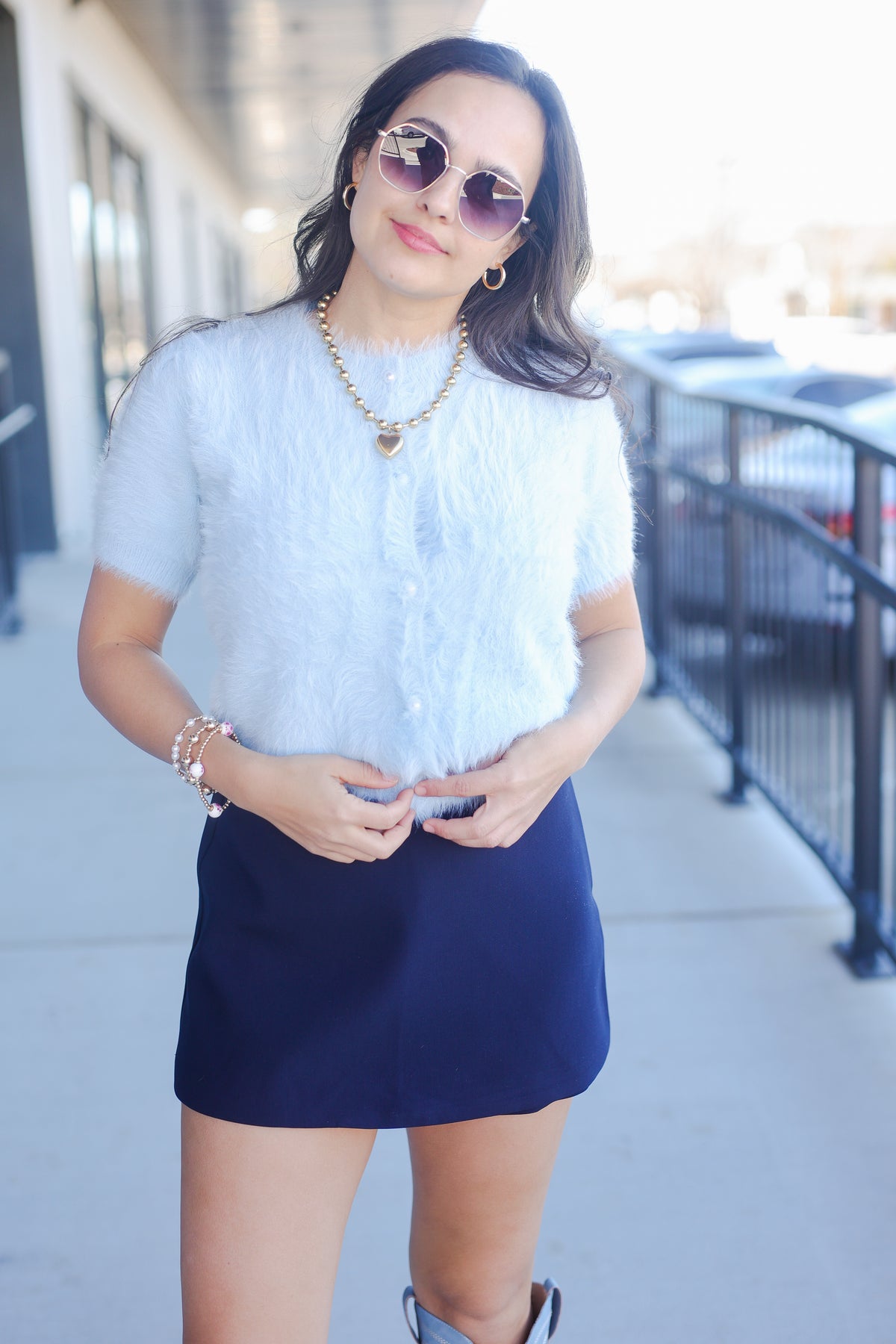 Woman wearing a light blue top and navy skirt outdoors.