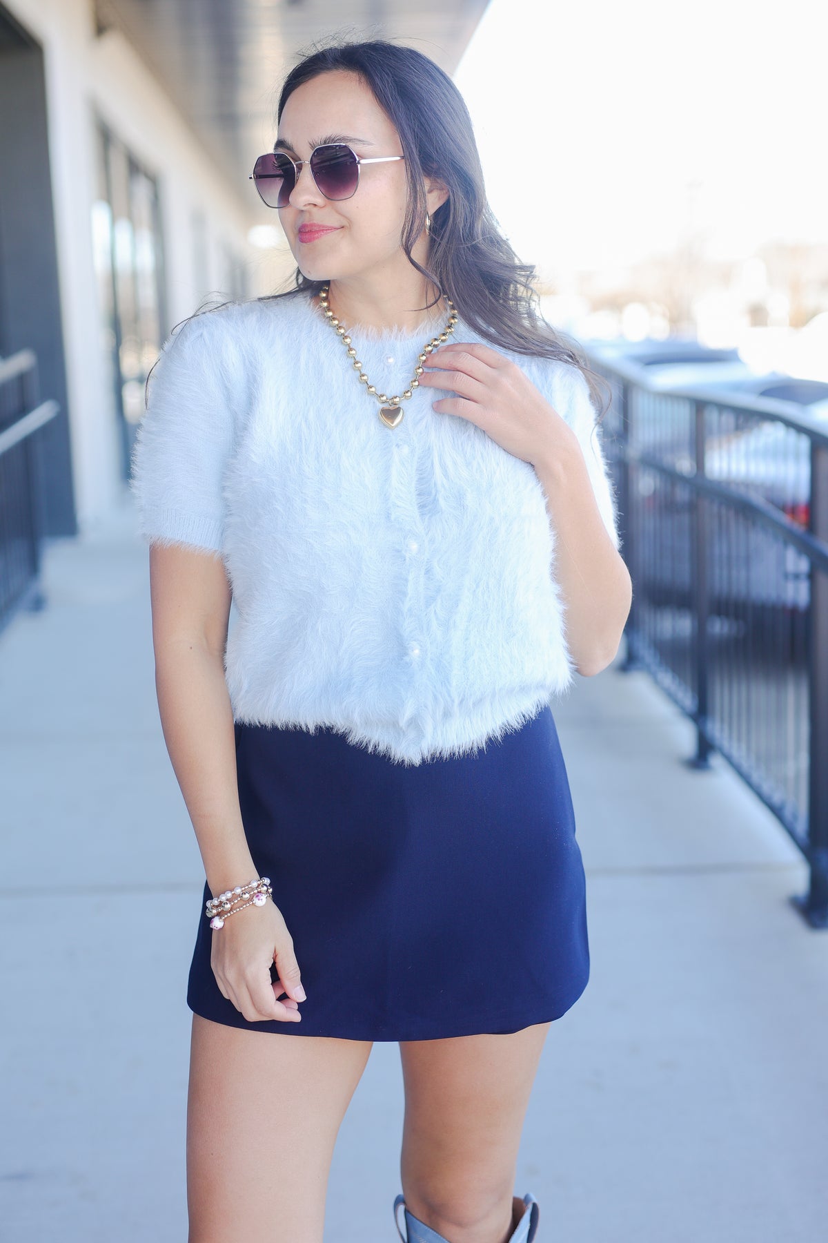 Woman wearing a light blue fluffy top and navy skirt outdoors.