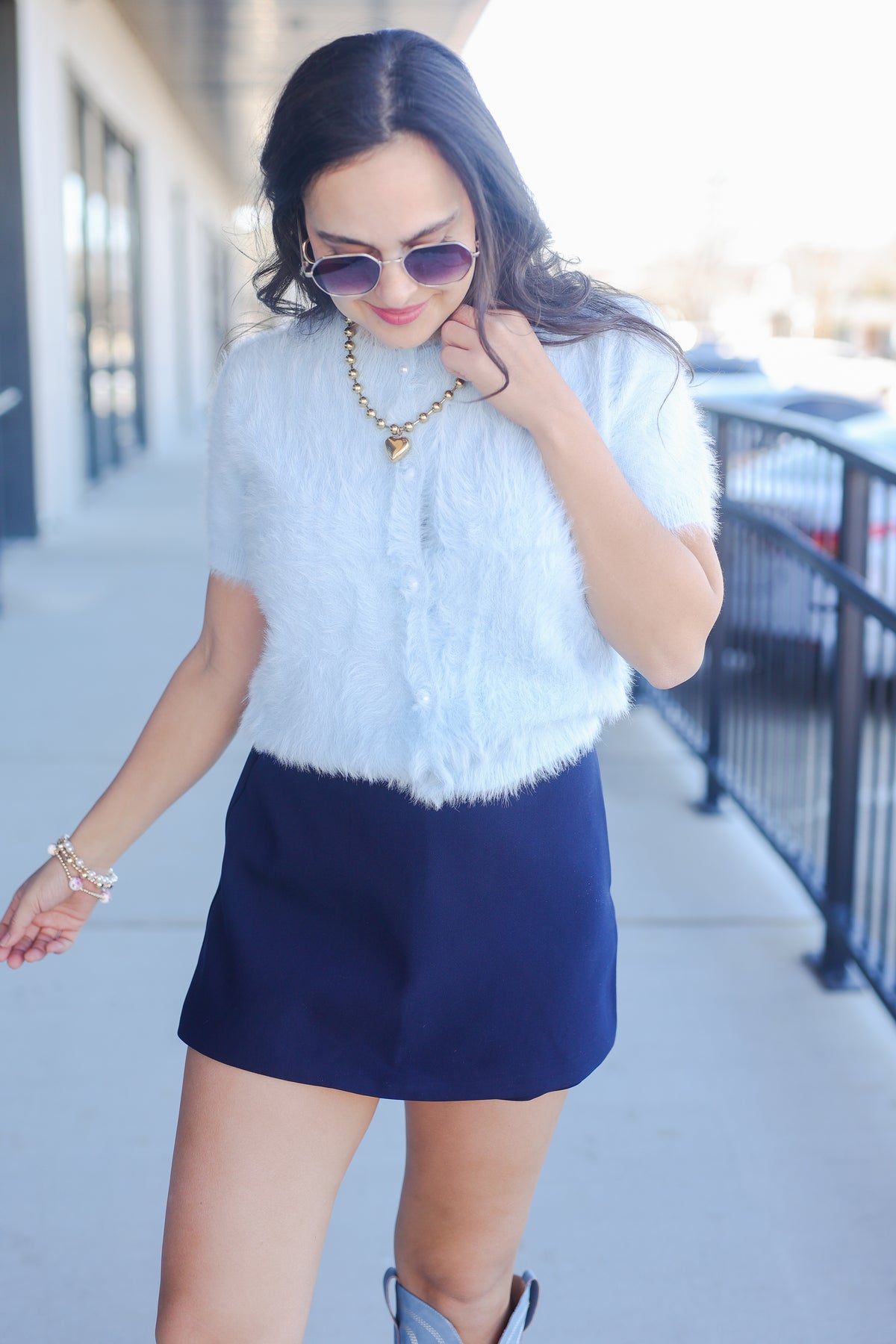 Woman wearing a white fur vest and blue skirt outdoors.