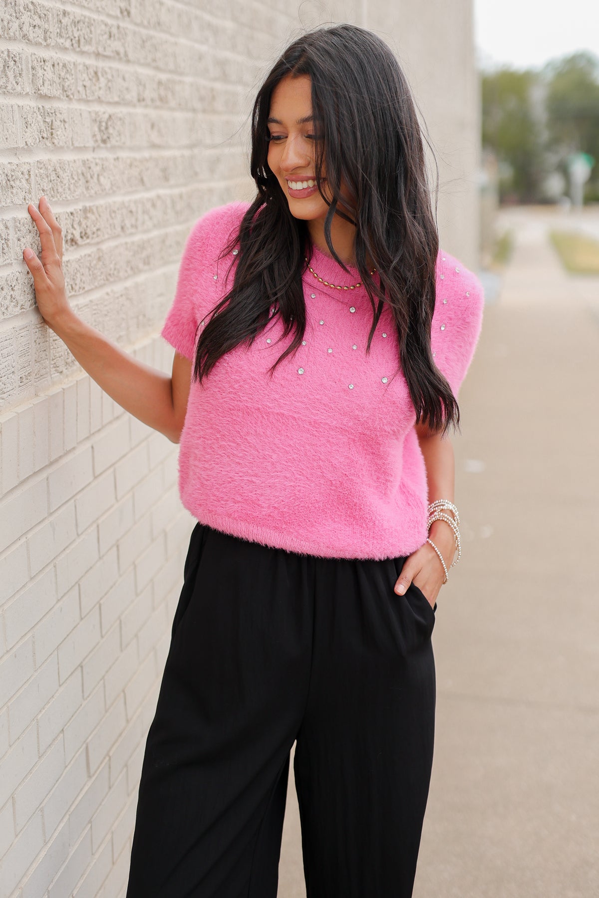 Brunette model wearing the Liora Pearl Knit Top –  Flamingo - and the Ellison pants in black with the toulouse flats on standing outside. Southern House Clothing