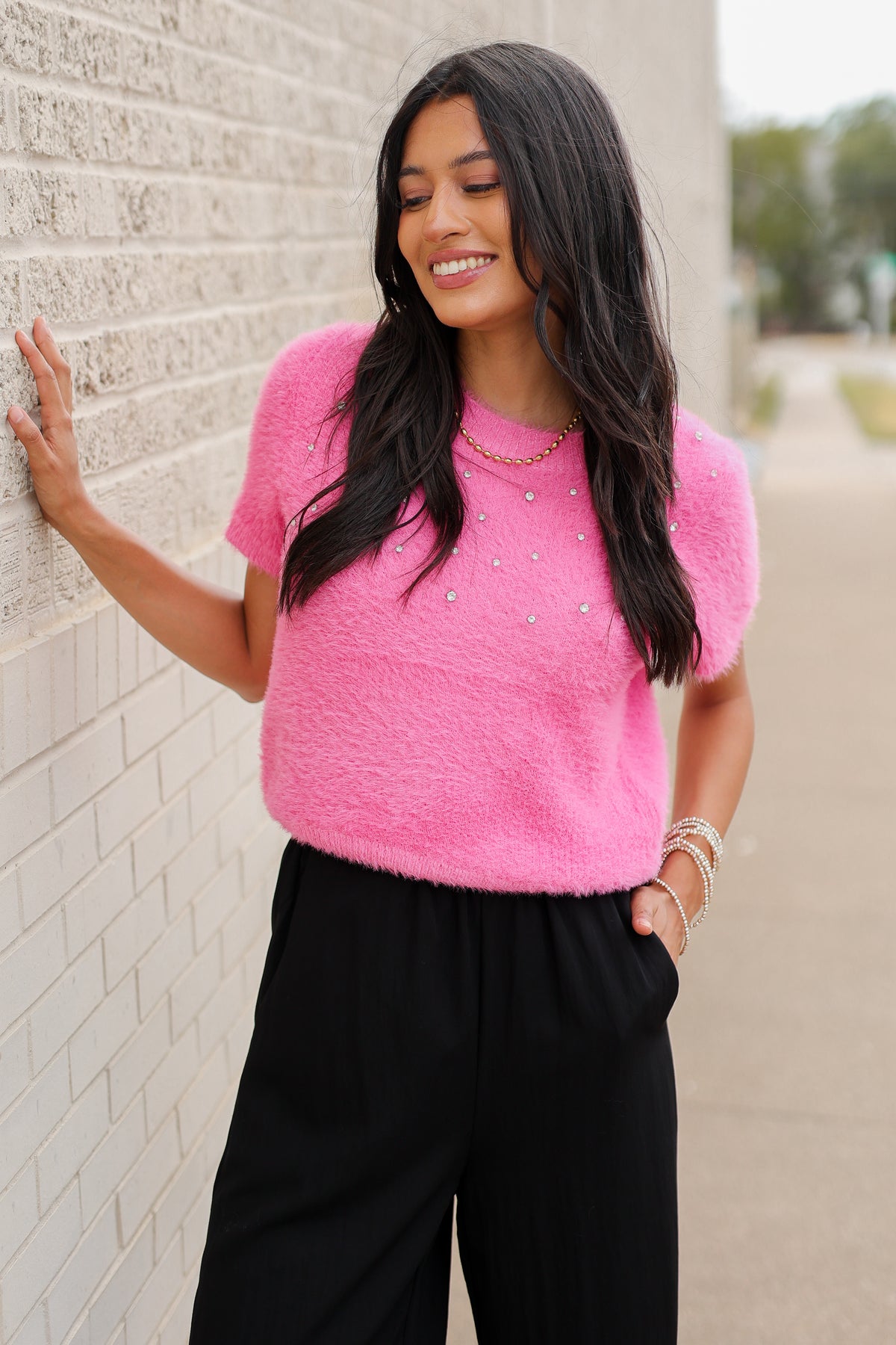 Brunette model wearing the Liora Pearl Knit Top –  Flamingo - and the Ellison pants in black with the toulouse flats on standing outside. Southern House Clothing