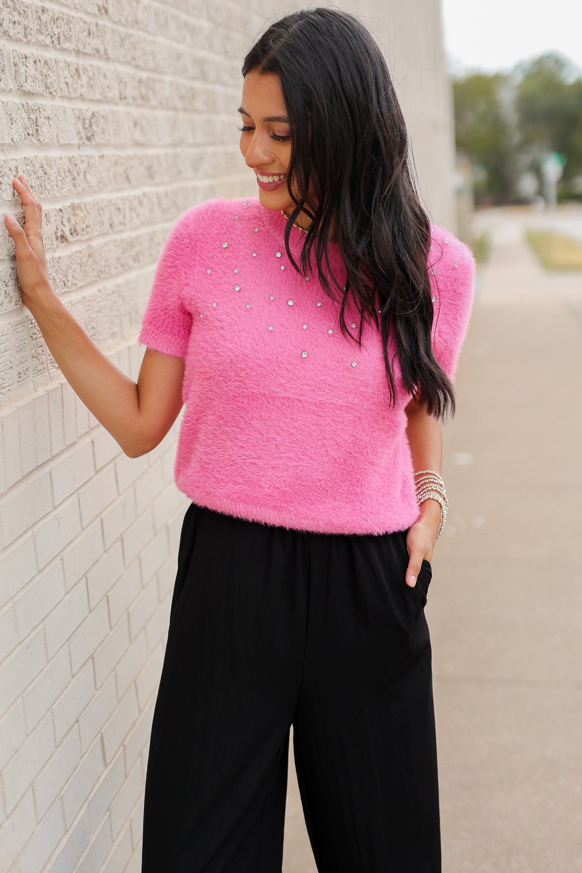 Brunette model wearing the Liora Pearl Knit Top –  Flamingo - and the Ellison pants in black with the toulouse flats on standing outside. Southern House Clothing