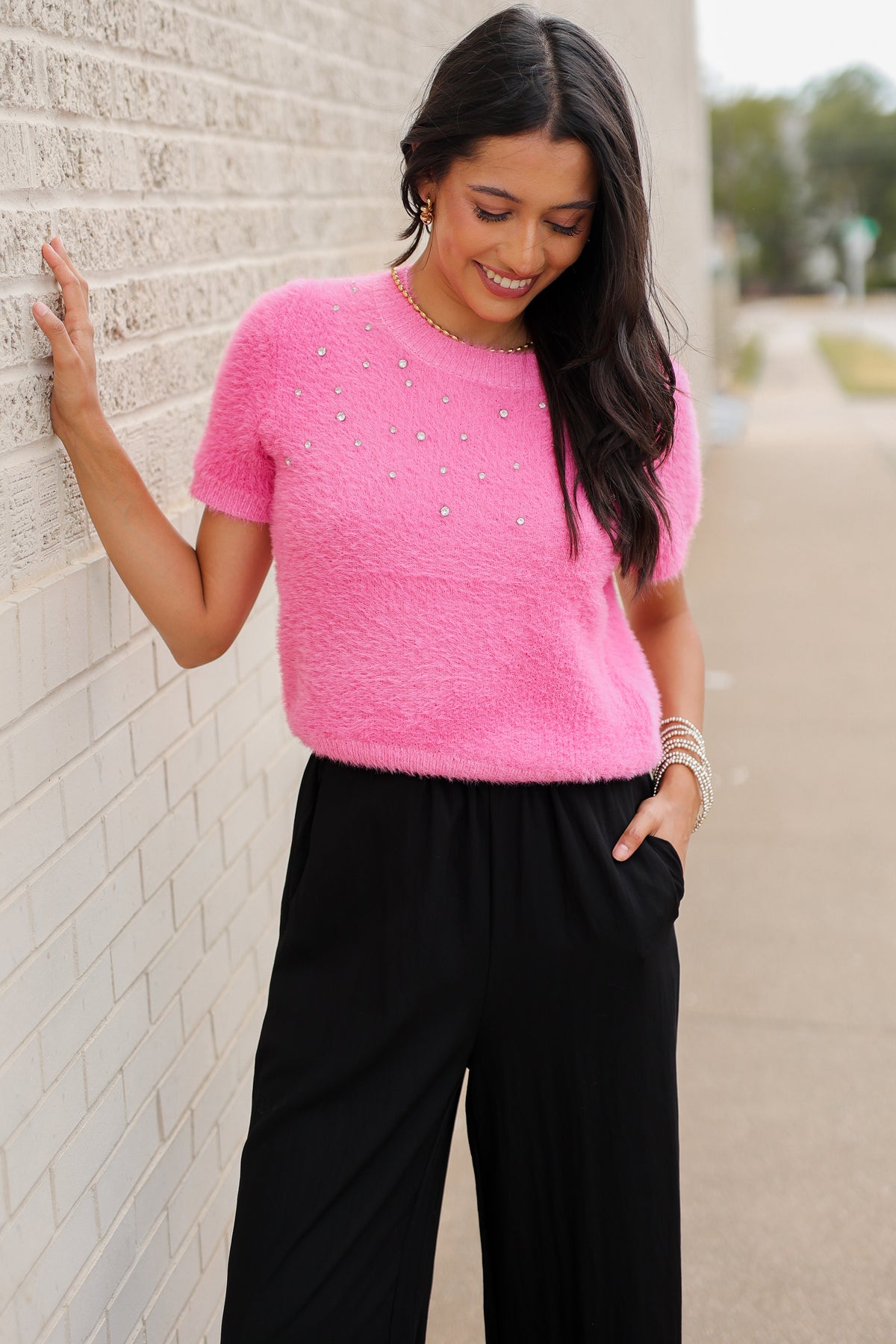 Brunette model wearing the Liora Pearl Knit Top –  Flamingo - and the Ellison pants in black with the toulouse flats on standing outside. Southern House Clothing