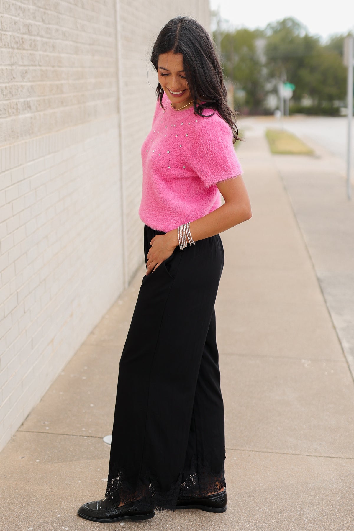 Brunette model wearing the Liora Pearl Knit Top –  Flamingo - and the Ellison pants in black with the toulouse flats on standing outside. Southern House Clothing