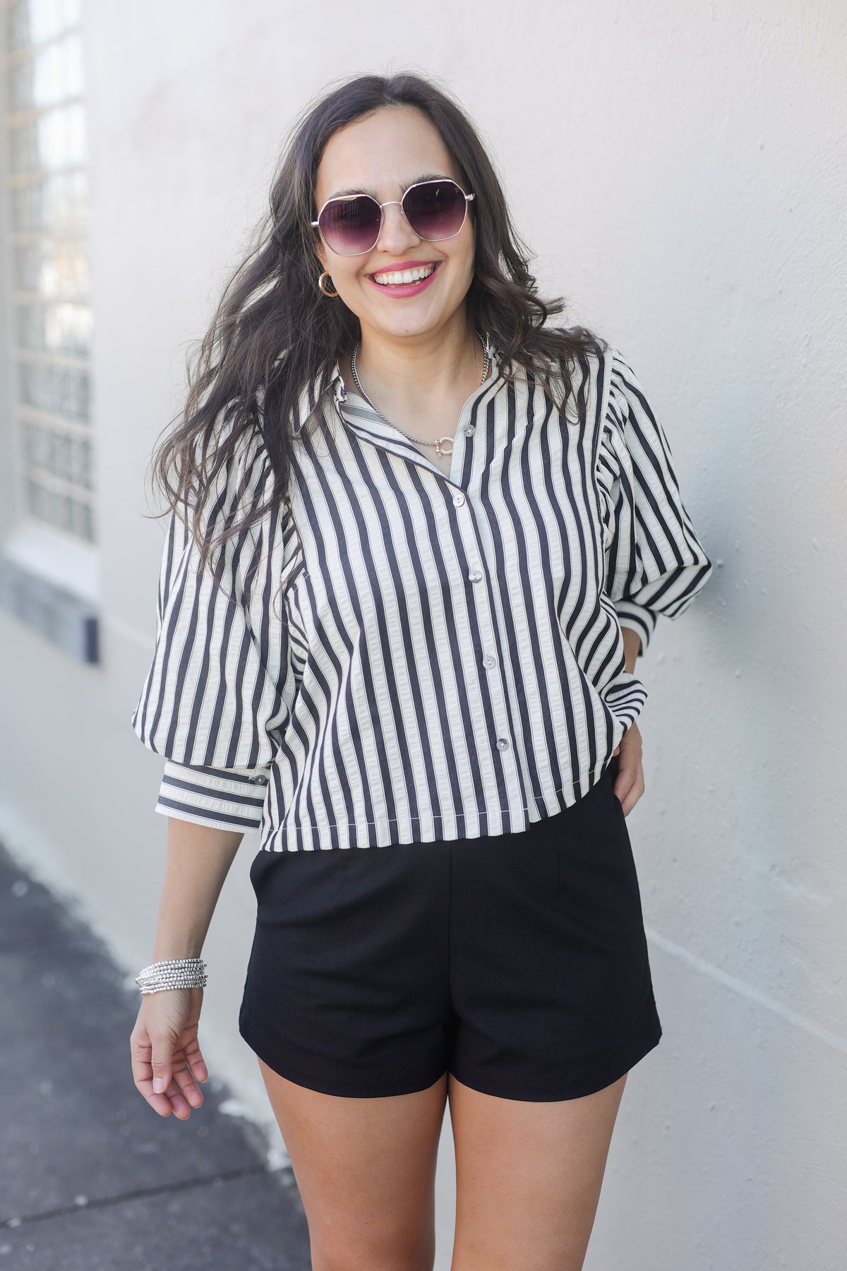Woman wearing a black and white striped shirt and black shorts against a white wall.