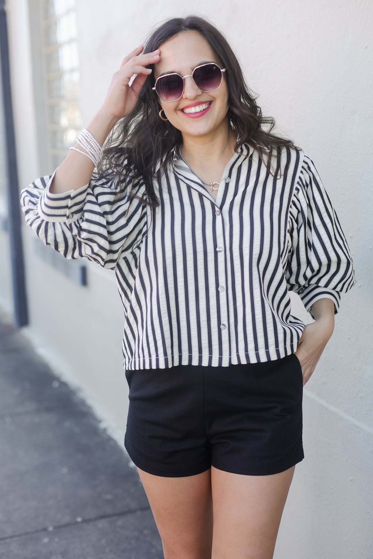 Woman wearing a black and white striped shirt and black shorts against a light-colored wall.