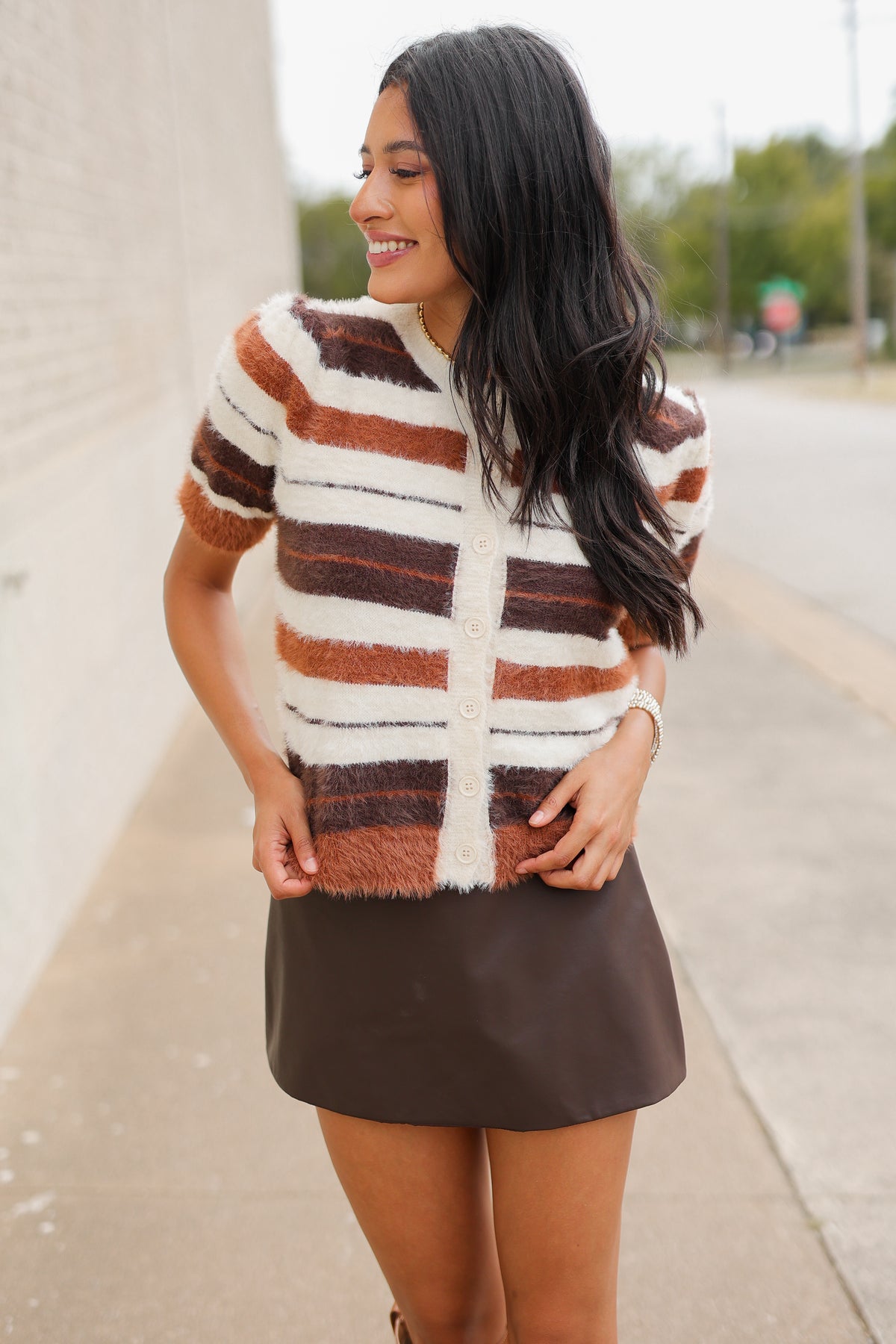 Brunette model standing outside wearing a brown multi colored sweater, brown skirt and light brown cowboys boots. Southern House Clothing