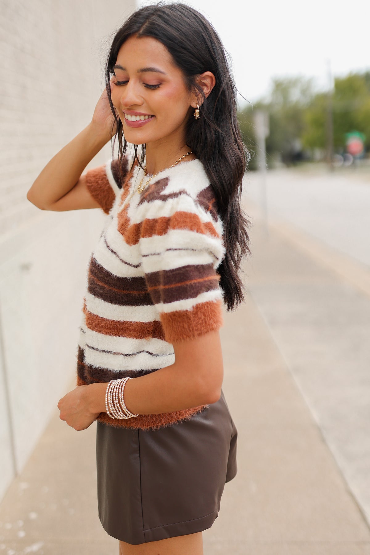 Brunette model standing outside wearing a brown multi colored sweater, brown skirt and light brown cowboys boots. Southern House Clothing