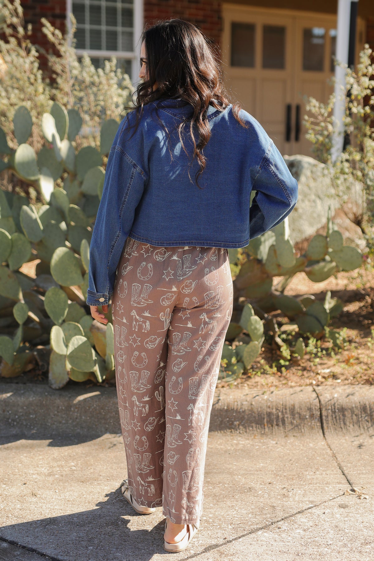 Person wearing a blue jacket and patterned pants standing in front of cacti.