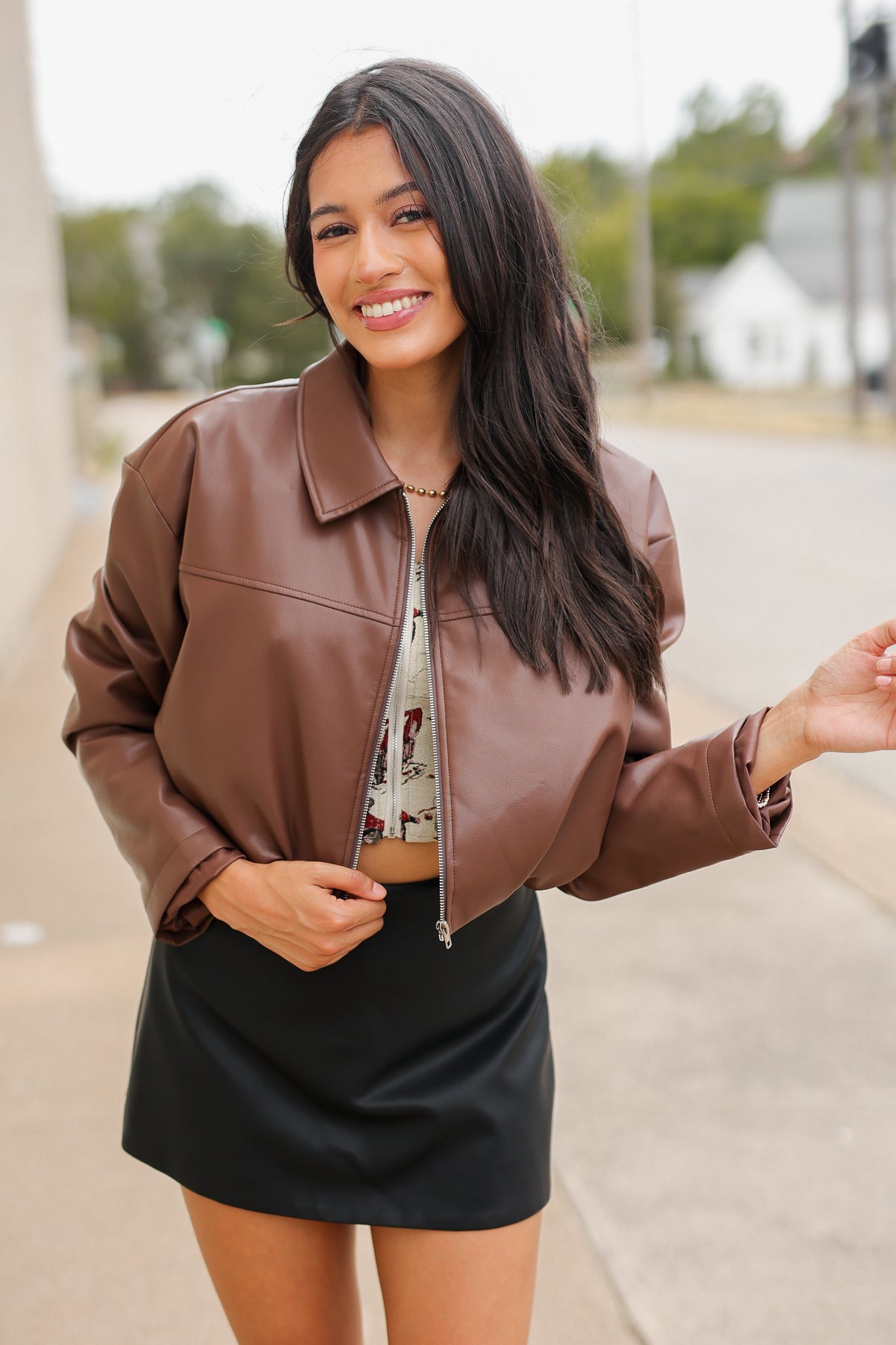 Model wearing the Riverton Cropped Faux Leather Jacket in Chocolate with the Briar black mini skirt and Amaya red western boots, featuring a relaxed silhouette and zip-front design. Southern House Clothing